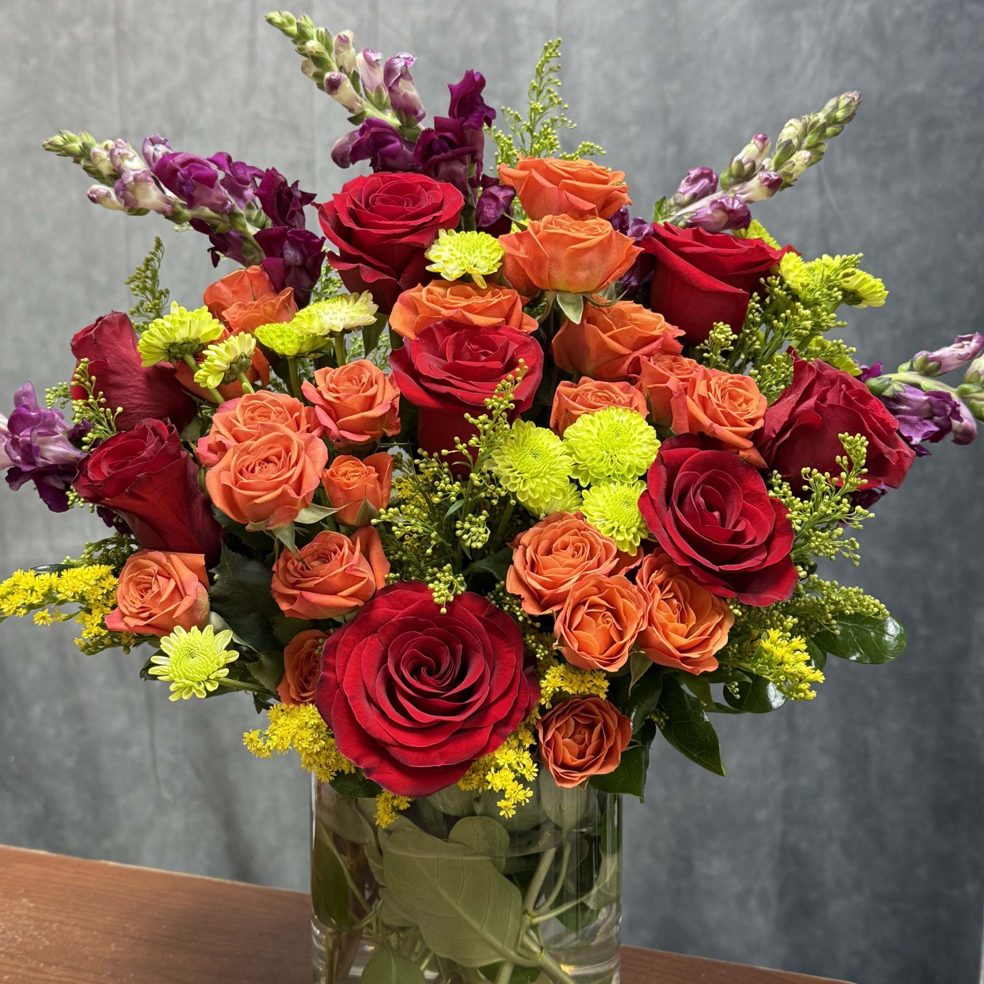 A lively blend of rich red roses, vibrant orange spray roses, green