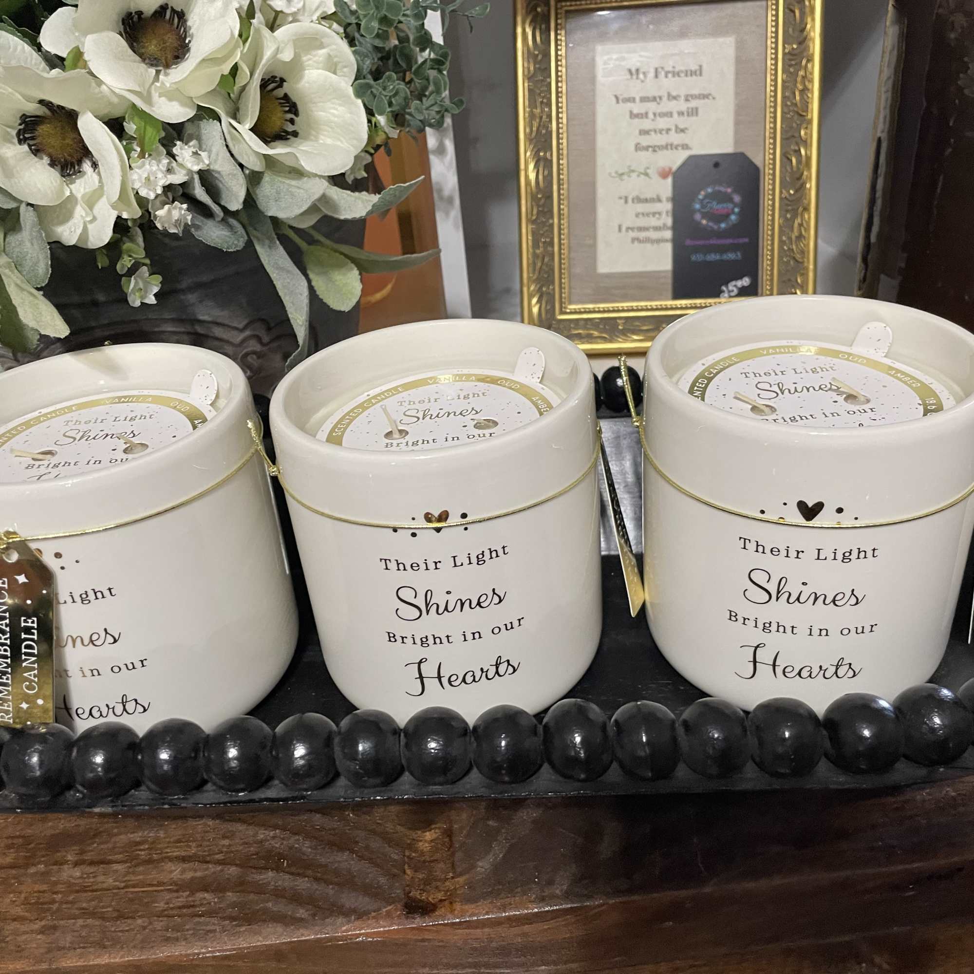 Three memorial candles in a tray with a white flower arrangement behind them.