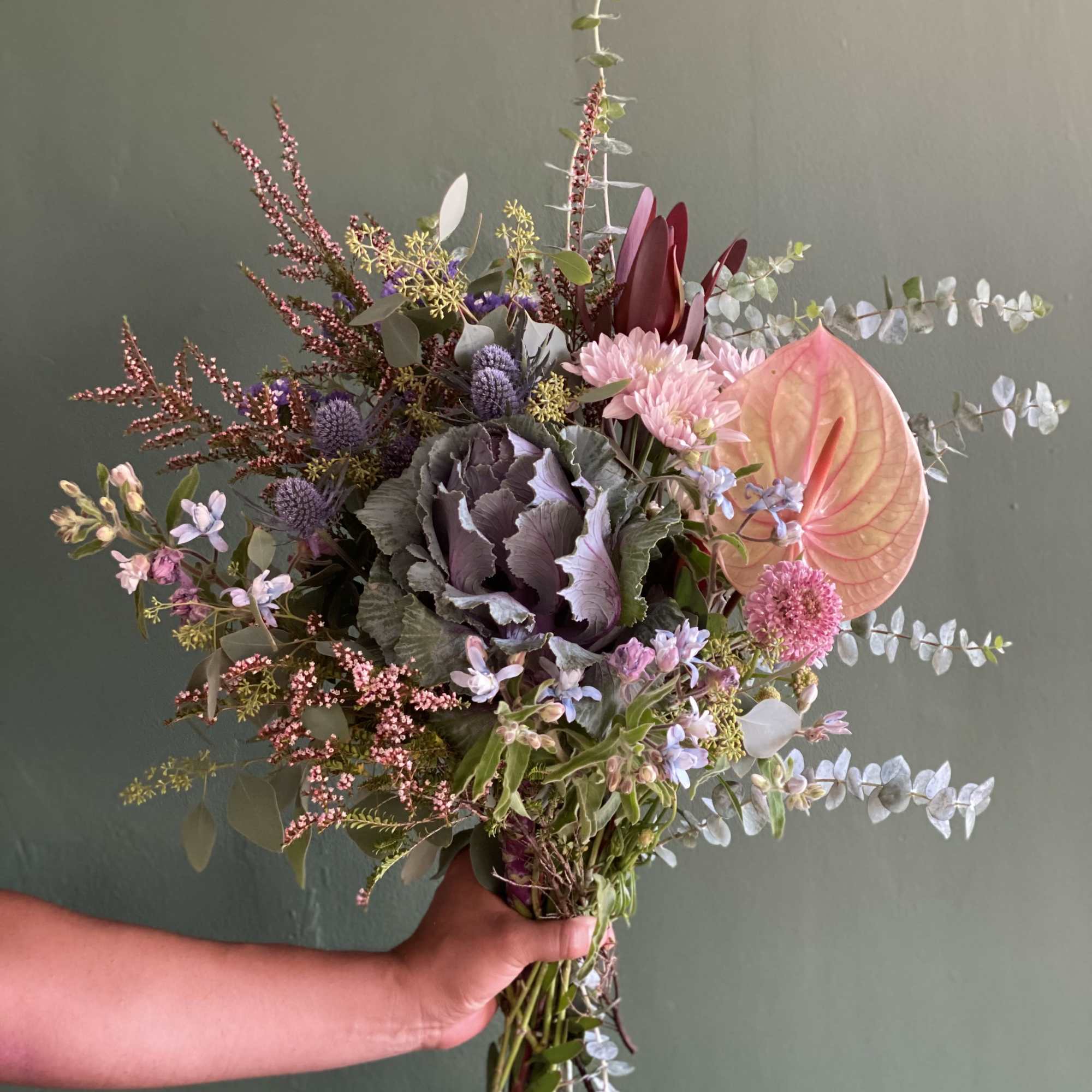 Handheld bouquet with pink anthurium, purple cabbage, and mixed blooms