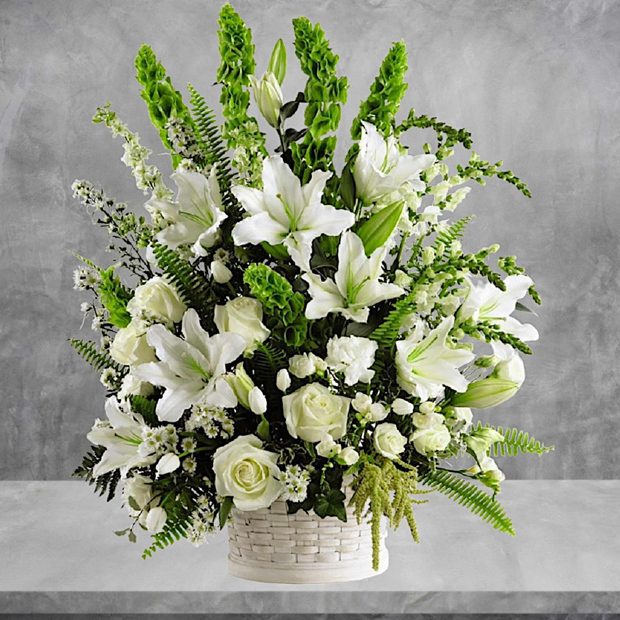 White lilies and roses arranged in a white basket with green accents