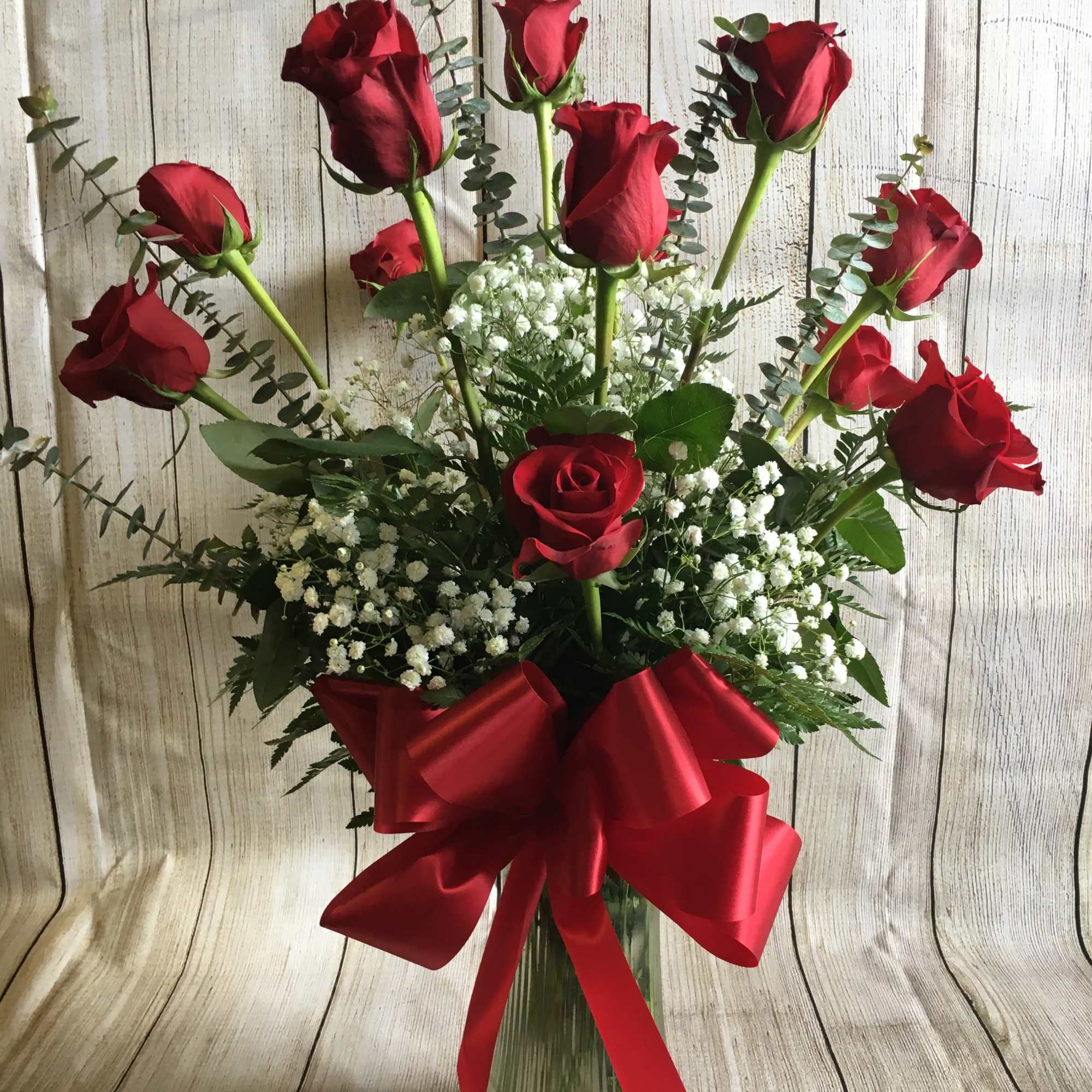 Red roses in a glass vase with baby's breath and a red ribbon