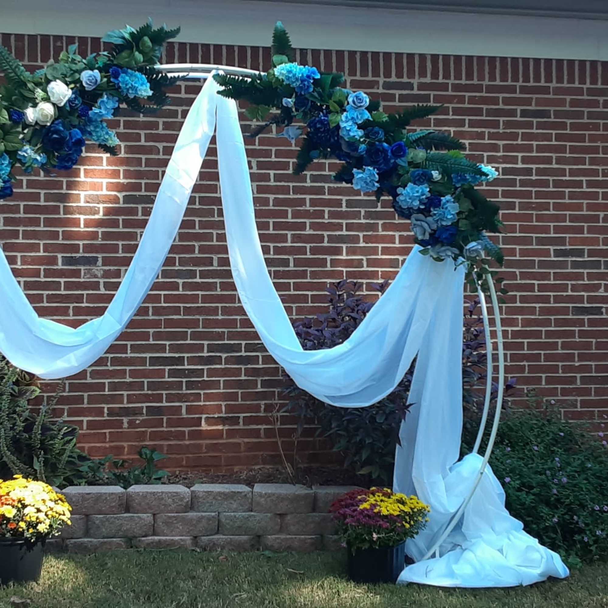 Blue floral arch with white draped fabric and potted flowers below