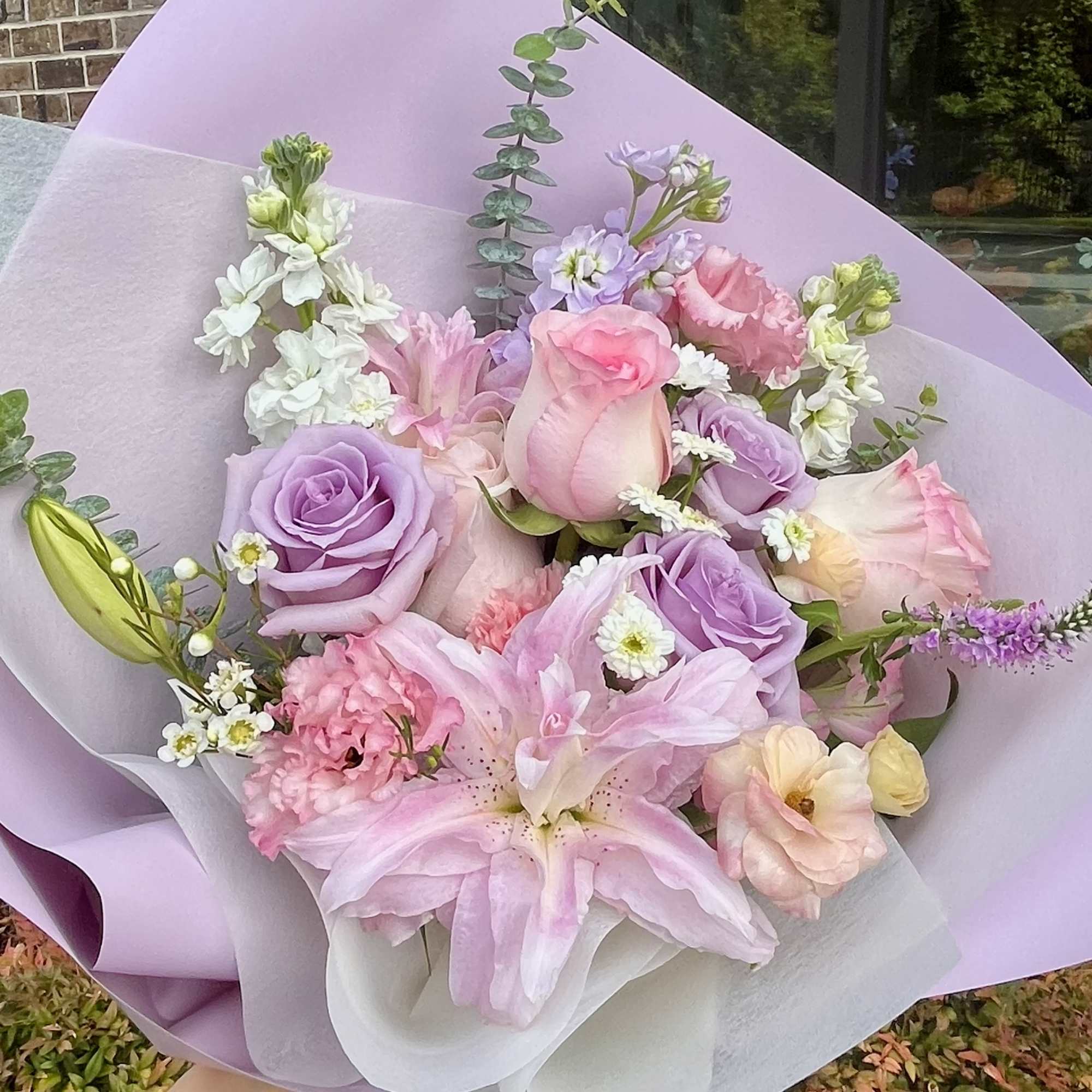 Pastel bouquet of pink and lavender roses with lilies wrapped in lilac paper