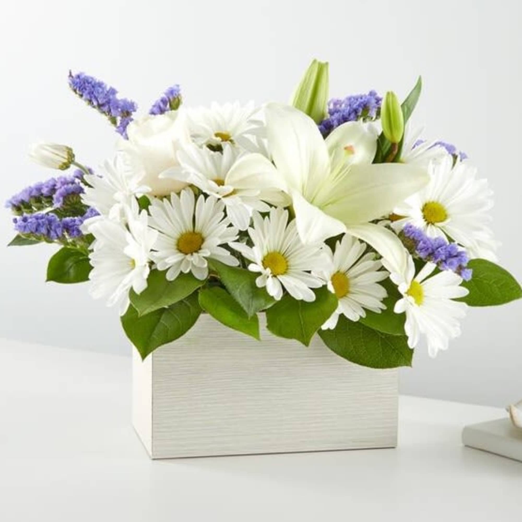 White daisies and lilies in a white box with purple accents