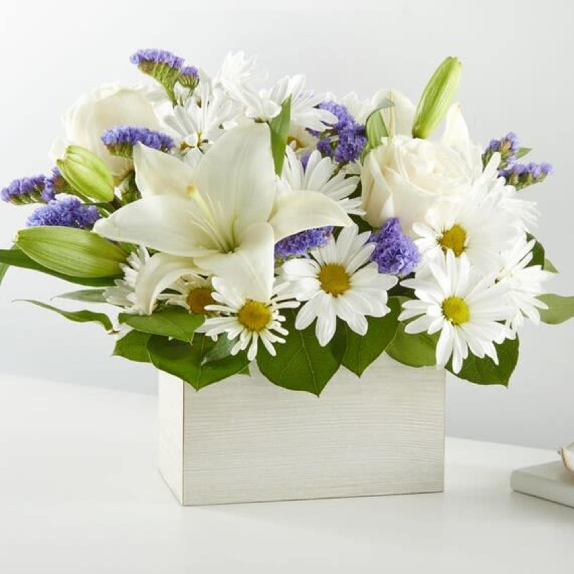 White lilies and daisies in a white box with purple filler flowers