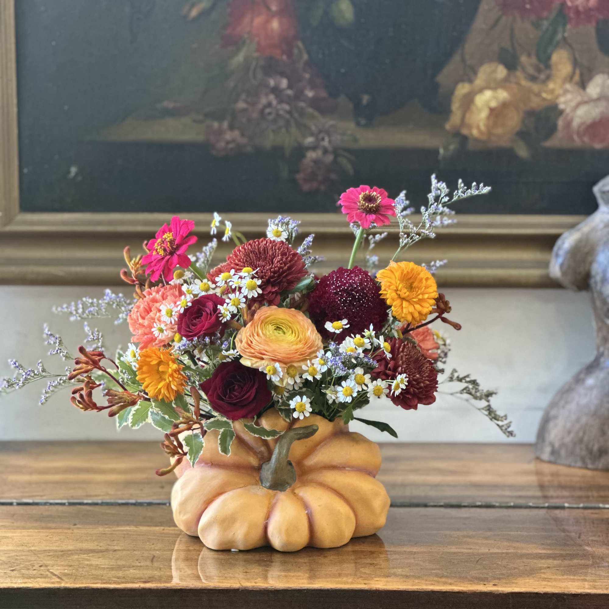 Autumn-toned flower arrangement in a pumpkin-shaped container on a wooden table