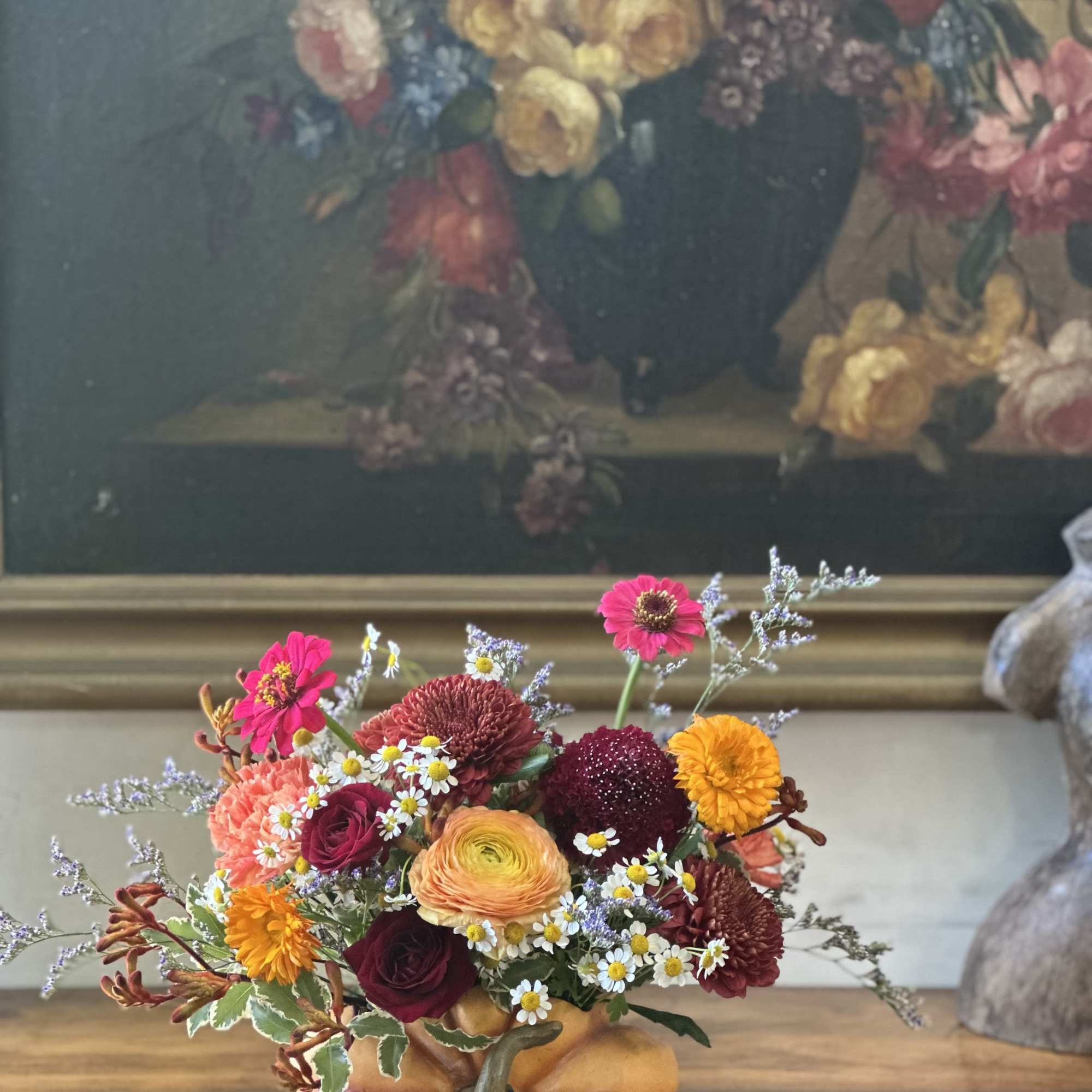 Low autumn bouquet of orange, burgundy, and yellow flowers arranged in a ceramic pumpkin container