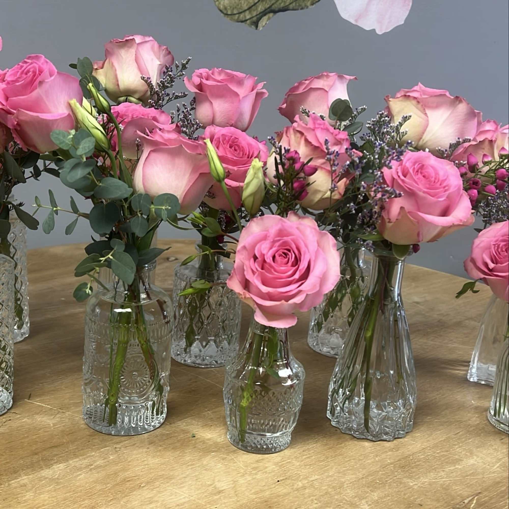 Group of clear glass bud vases with pink roses on a wooden table