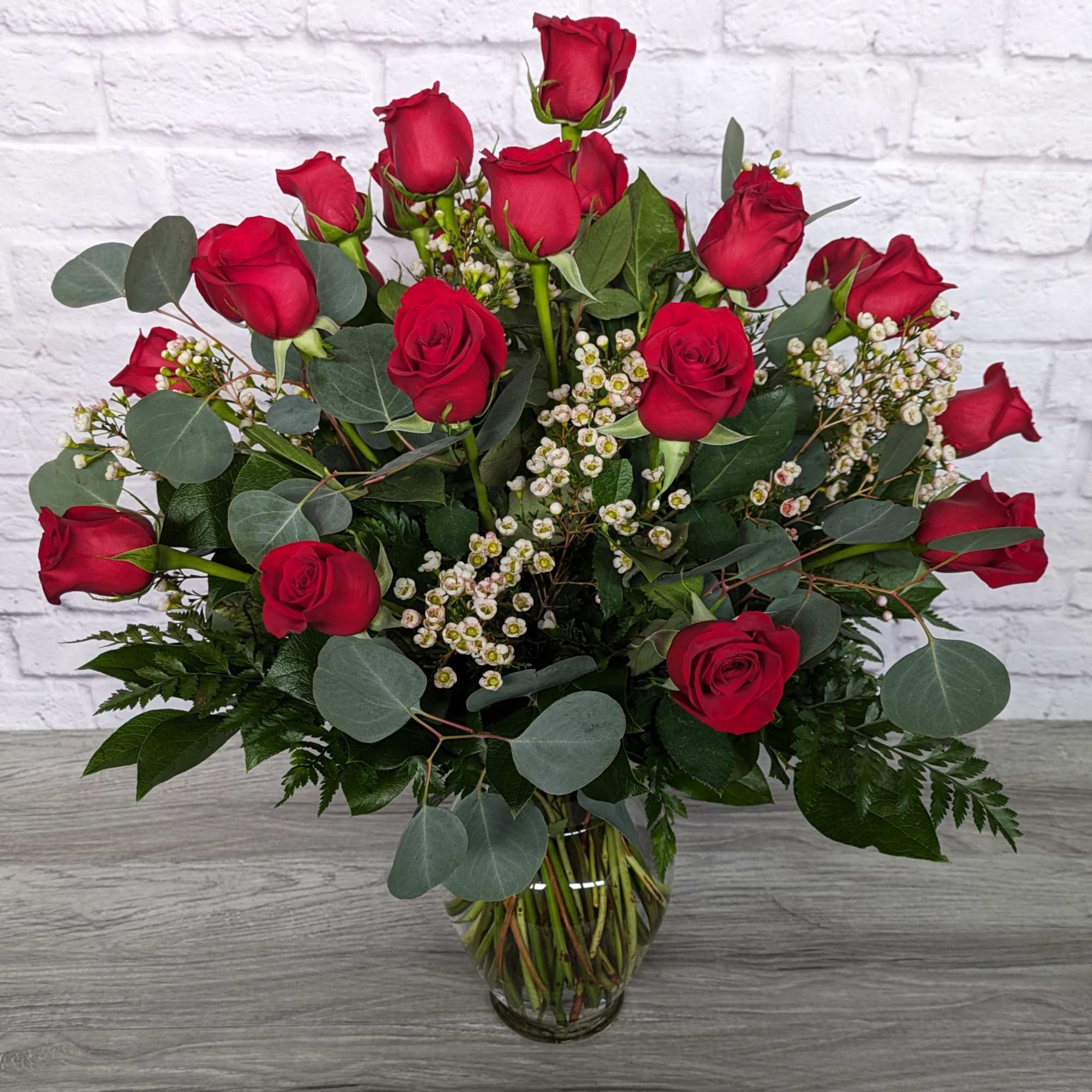 Red roses arranged in a clear glass vase with white filler flowers