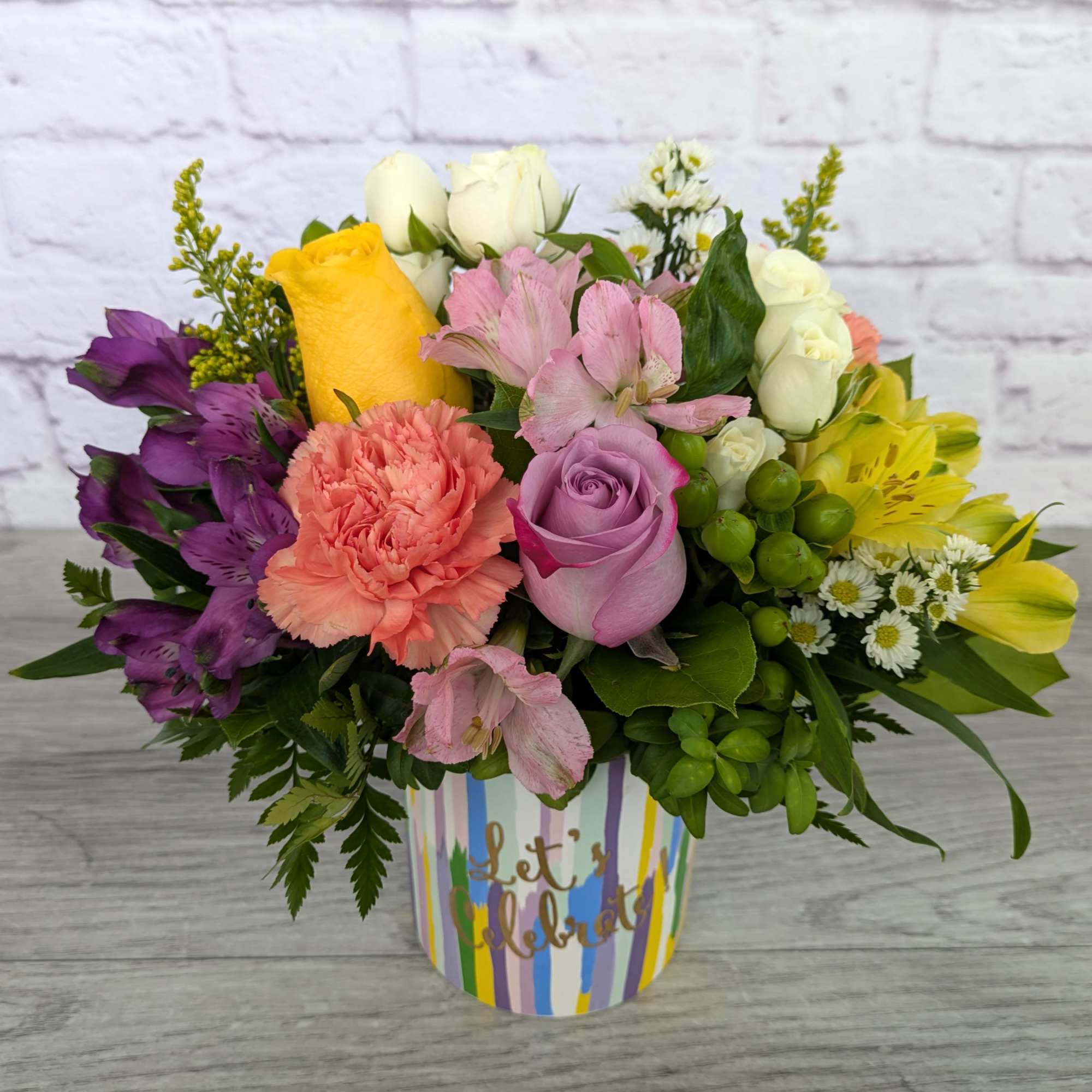 Colorful mixed bouquet in a striped container with roses and carnations