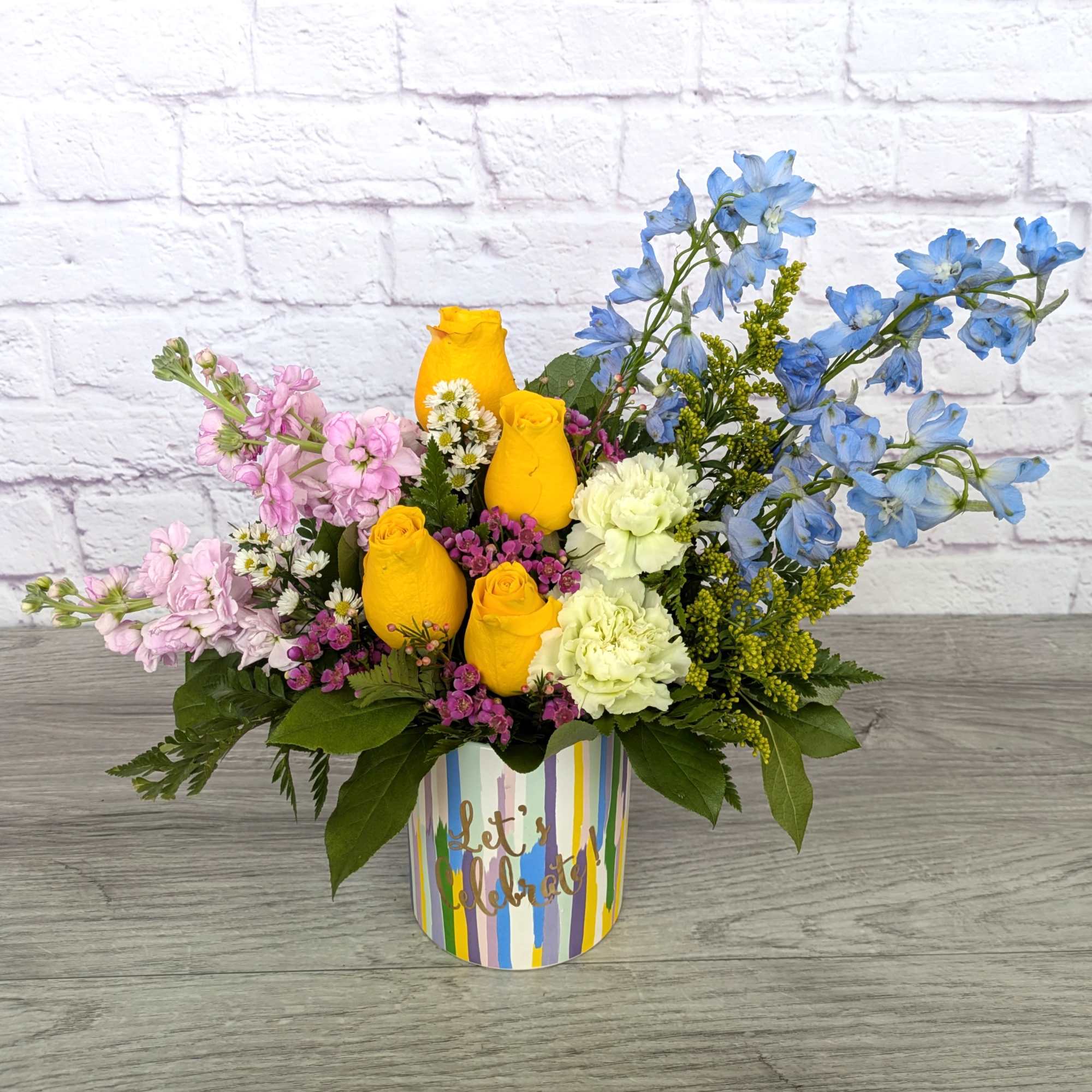 Colorful flower arrangement in a striped gift box with yellow roses and blue blooms