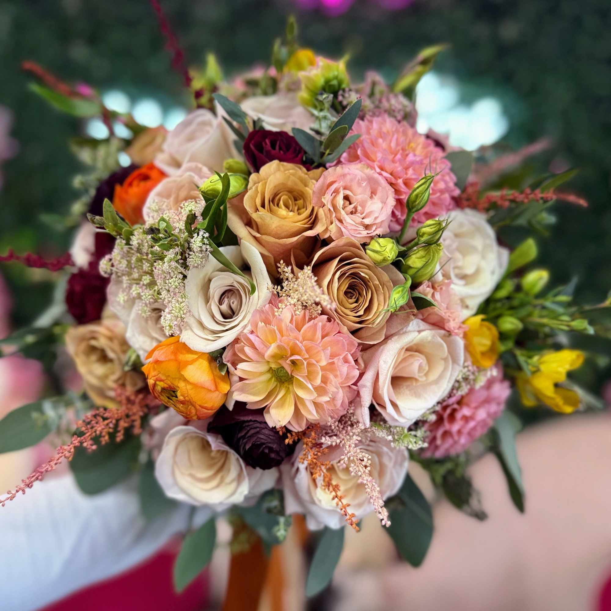 Handheld bouquet of roses and dahlias in pink, peach, and cream