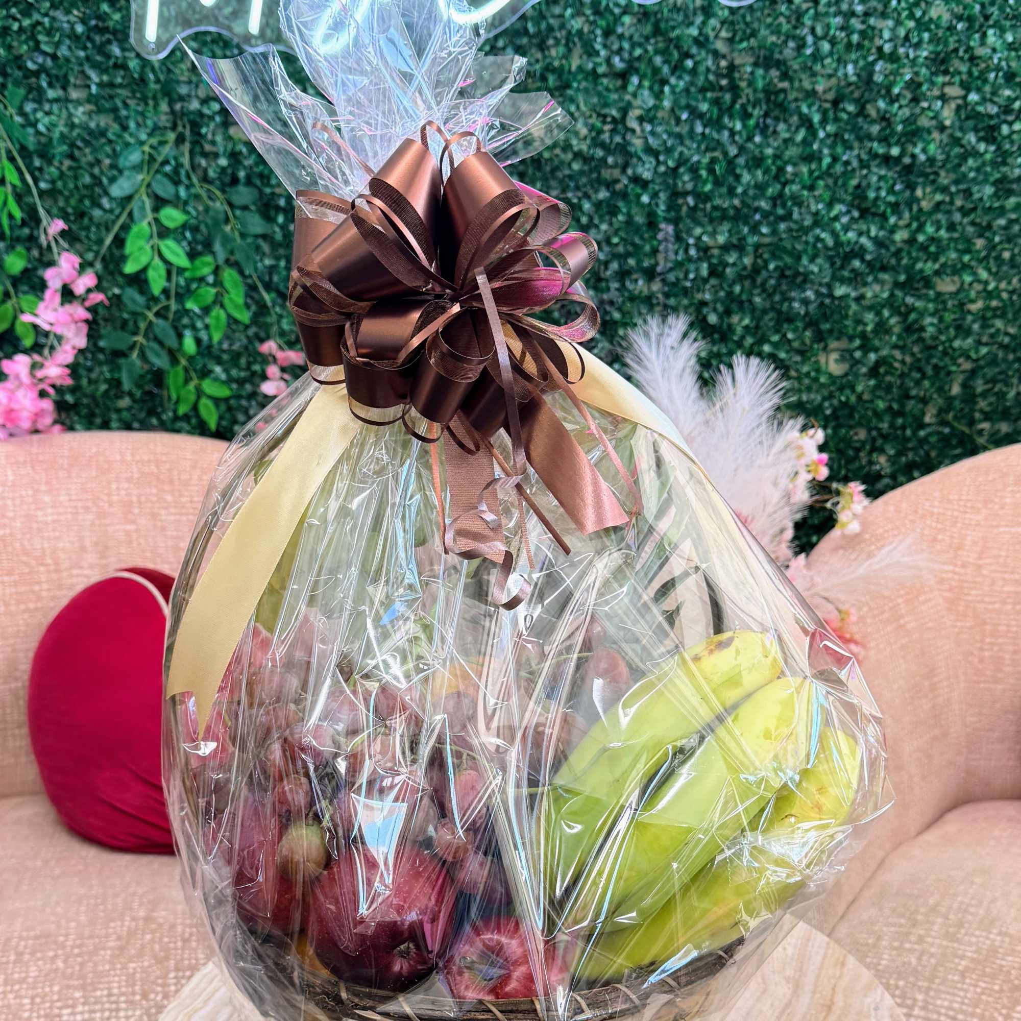 Wrapped gift basket with flowers and fruit, topped with a brown ribbon bow