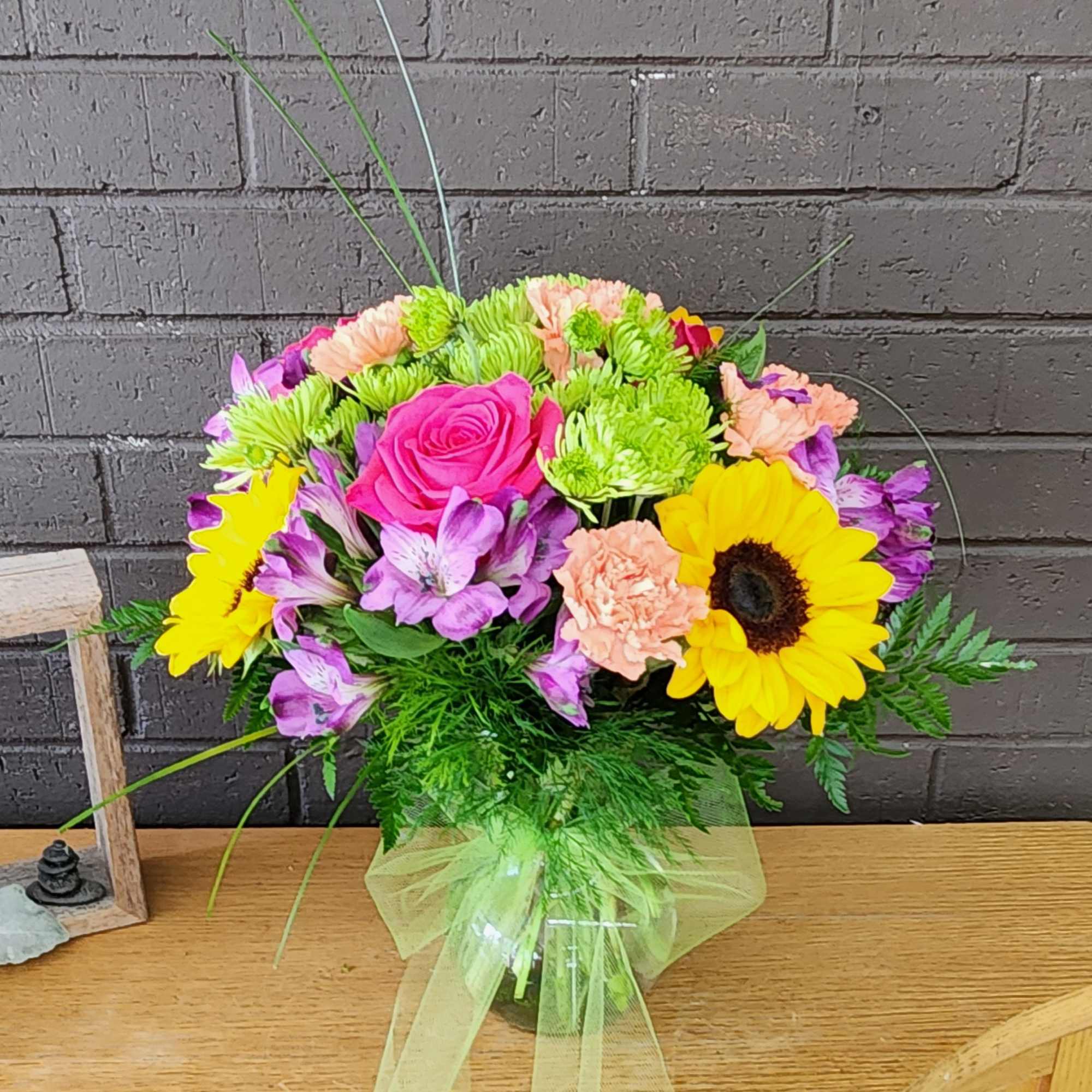 Mixed bouquet with pink roses, sunflowers, and purple flowers in a glass vase