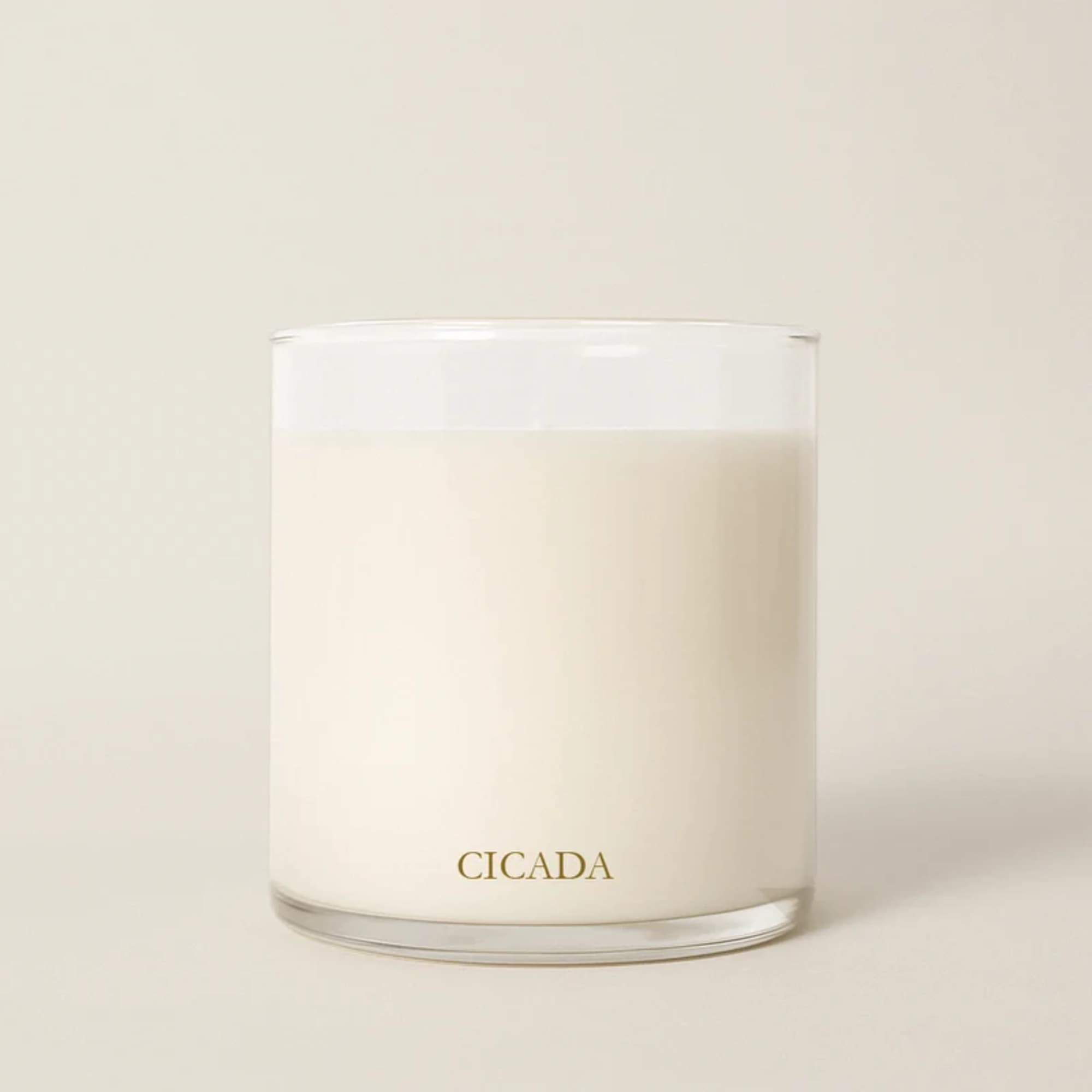 White candle in a clear glass tumbler with CICADA printed on it
