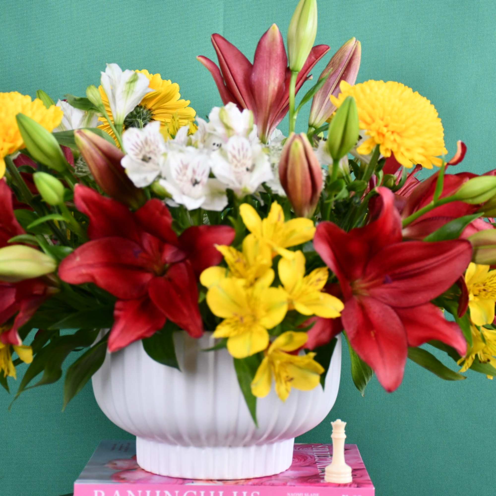 Mixed bouquet of red lilies, yellow daisies, and white alstroemeria in a white vase
