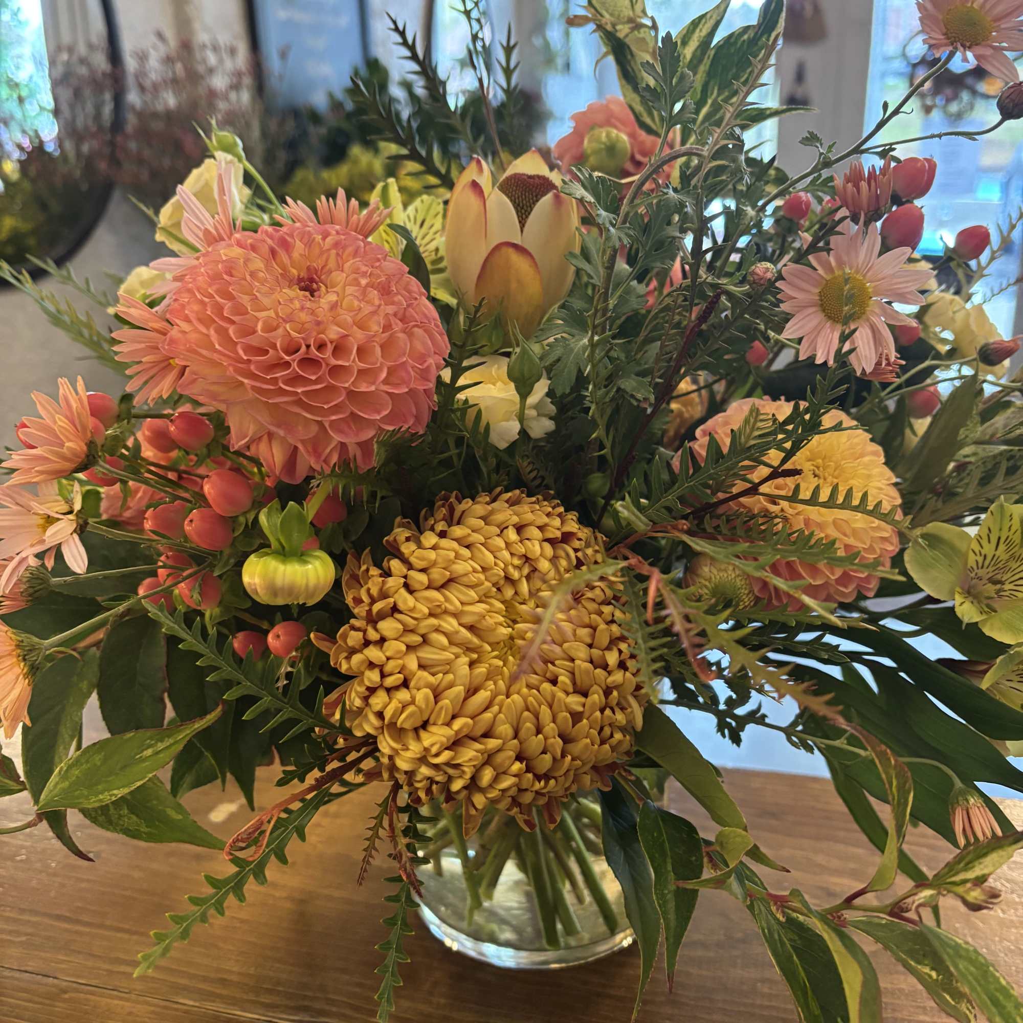 Mixed bouquet of peach, yellow, and pink flowers in a clear glass vase