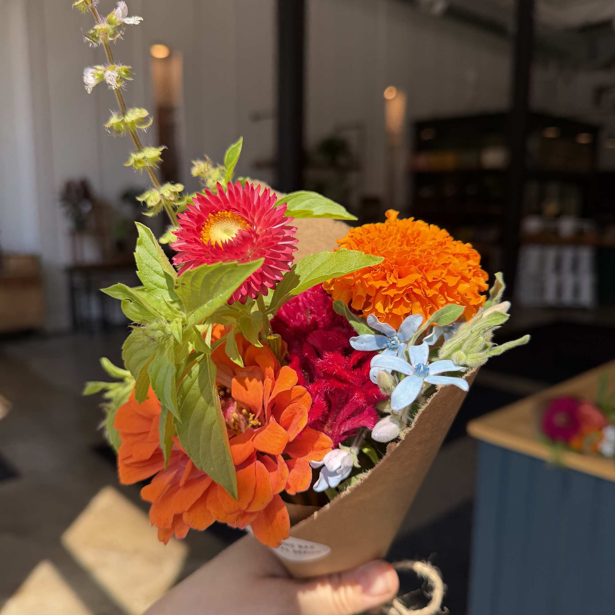 Small bouquet of orange and pink flowers wrapped in brown paper