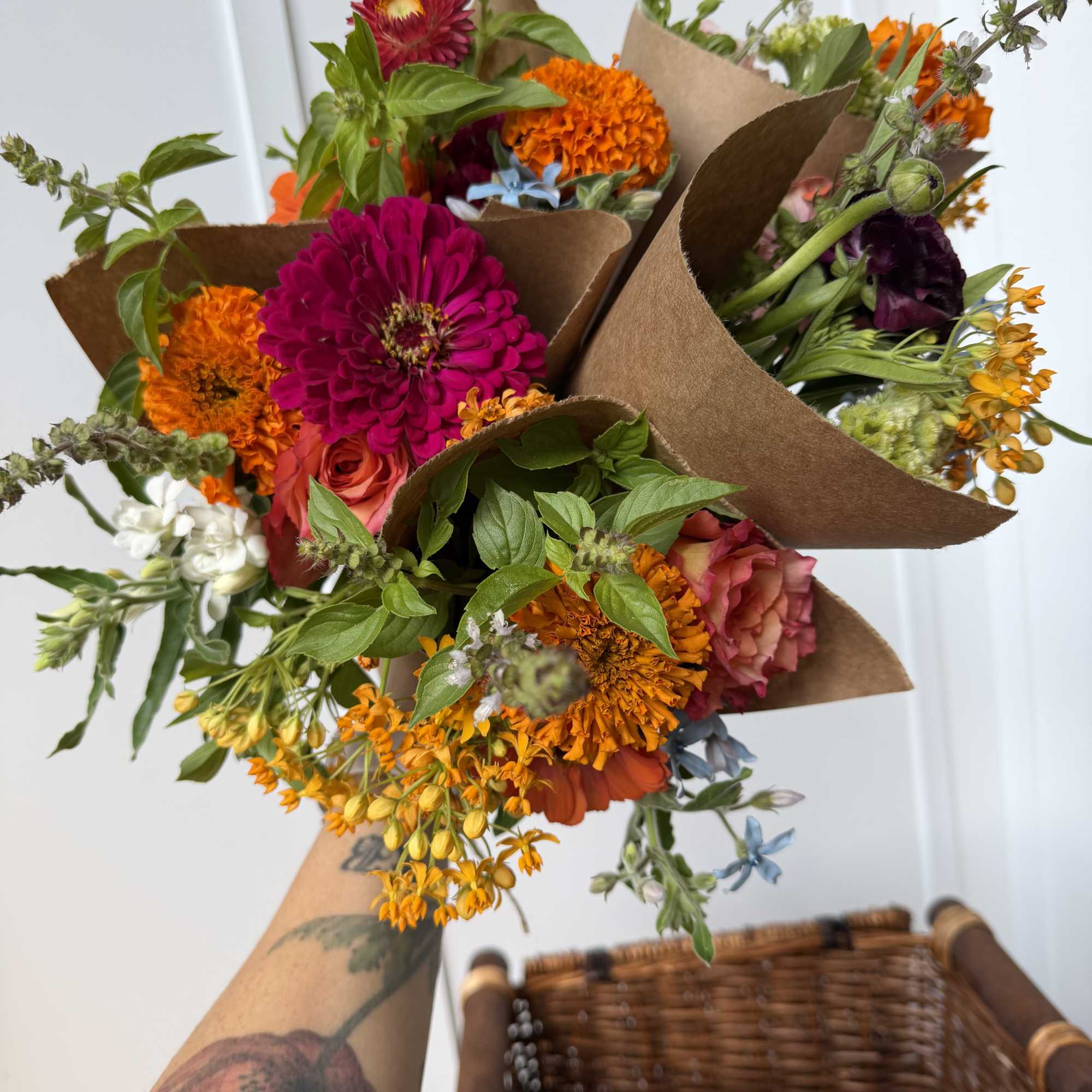 Handheld mixed bouquets with bright orange and magenta flowers wrapped in brown paper