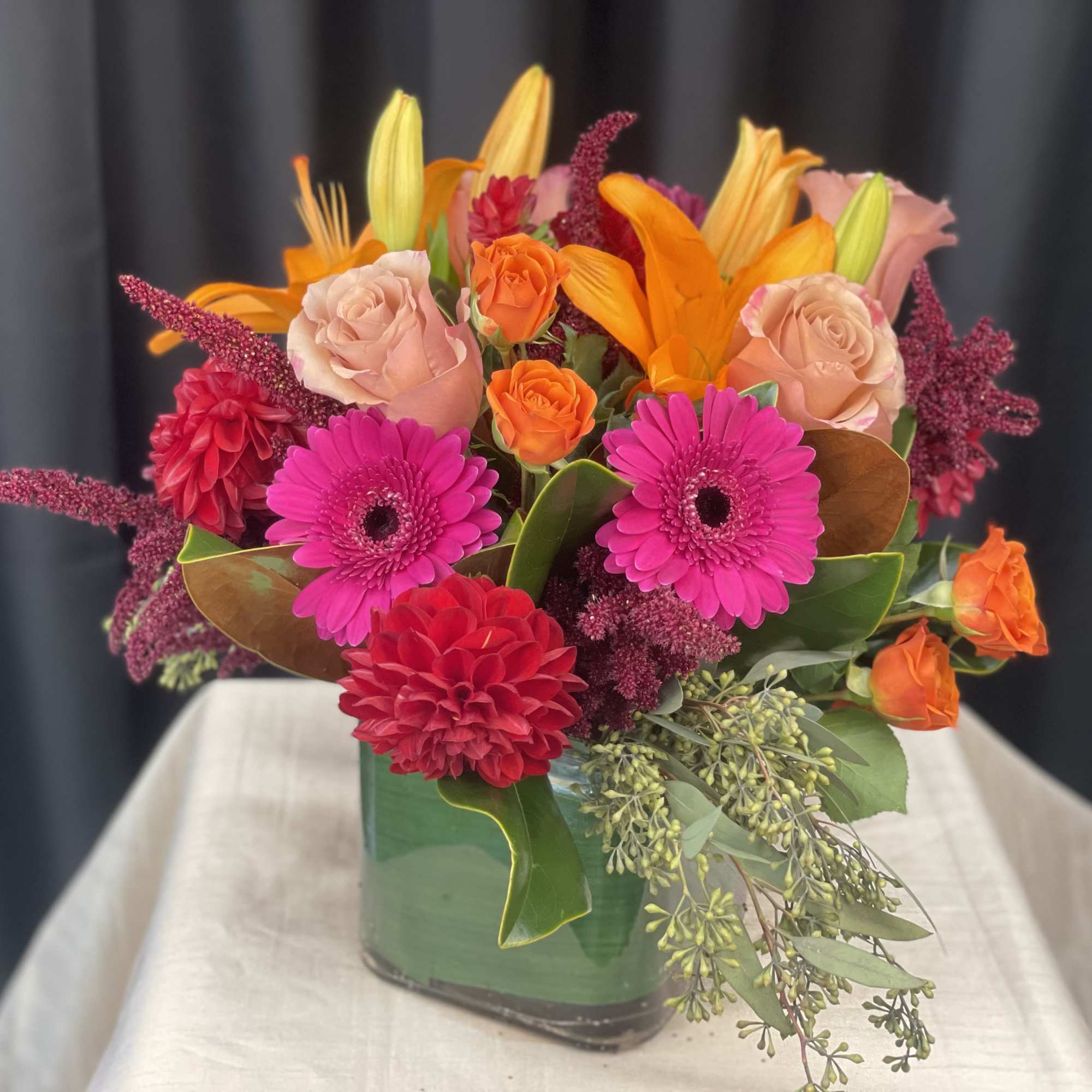 Bright mixed bouquet in a square glass vase with pink, orange, and red flowers