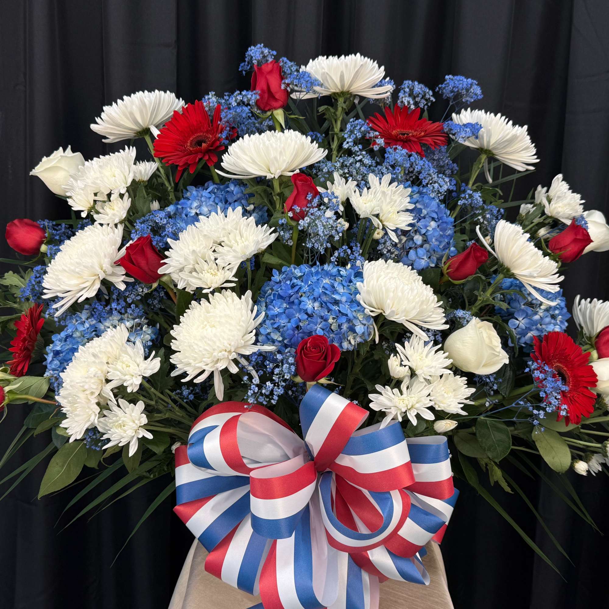 Large red, white, and blue floral arrangement with a ribbon bow