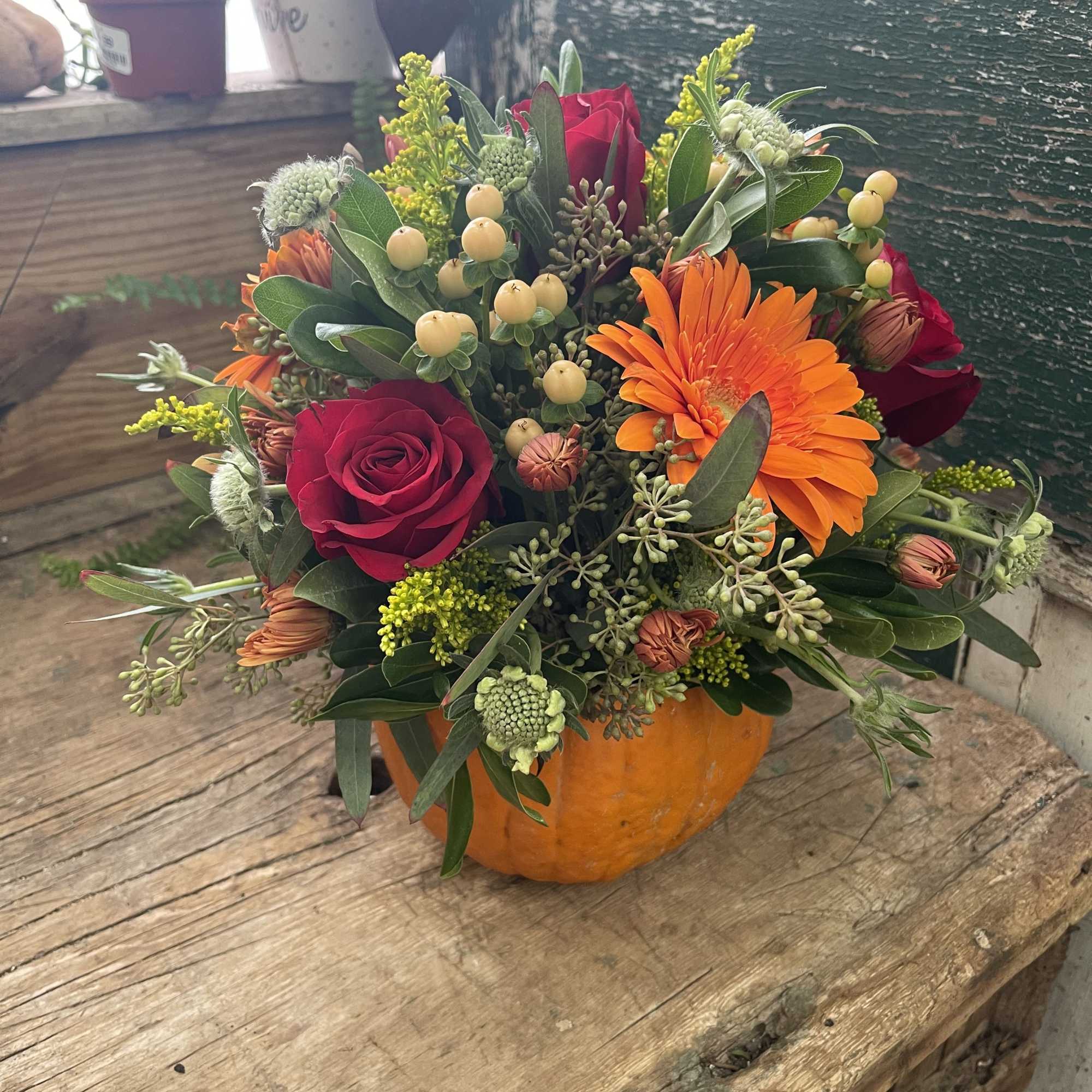 Mixed bouquet in a pumpkin container with red roses and orange gerbera daisies