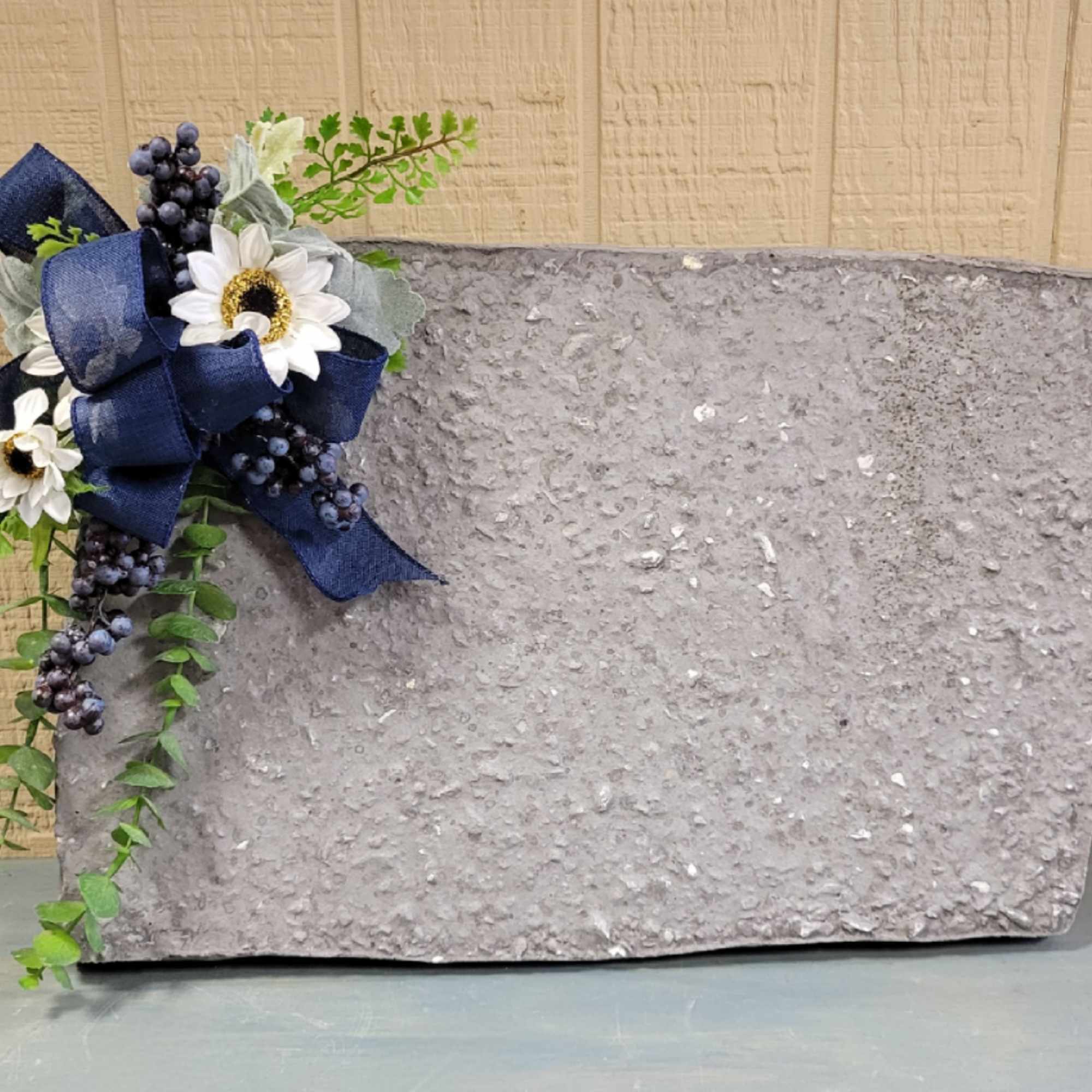 Gray stone memorial plaque with a navy ribbon and white daisies