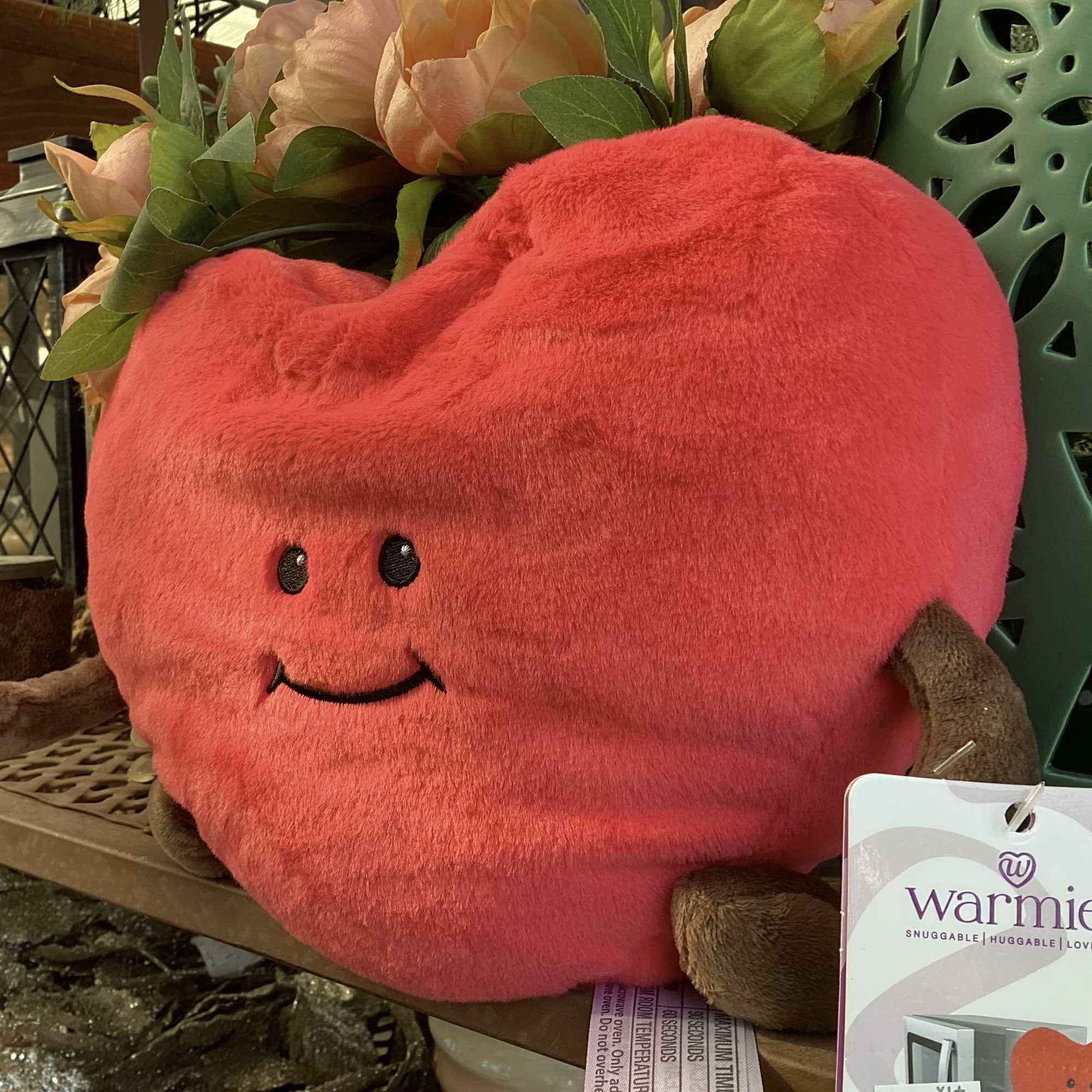 Pink plush heart with a smiling face beside flowers
