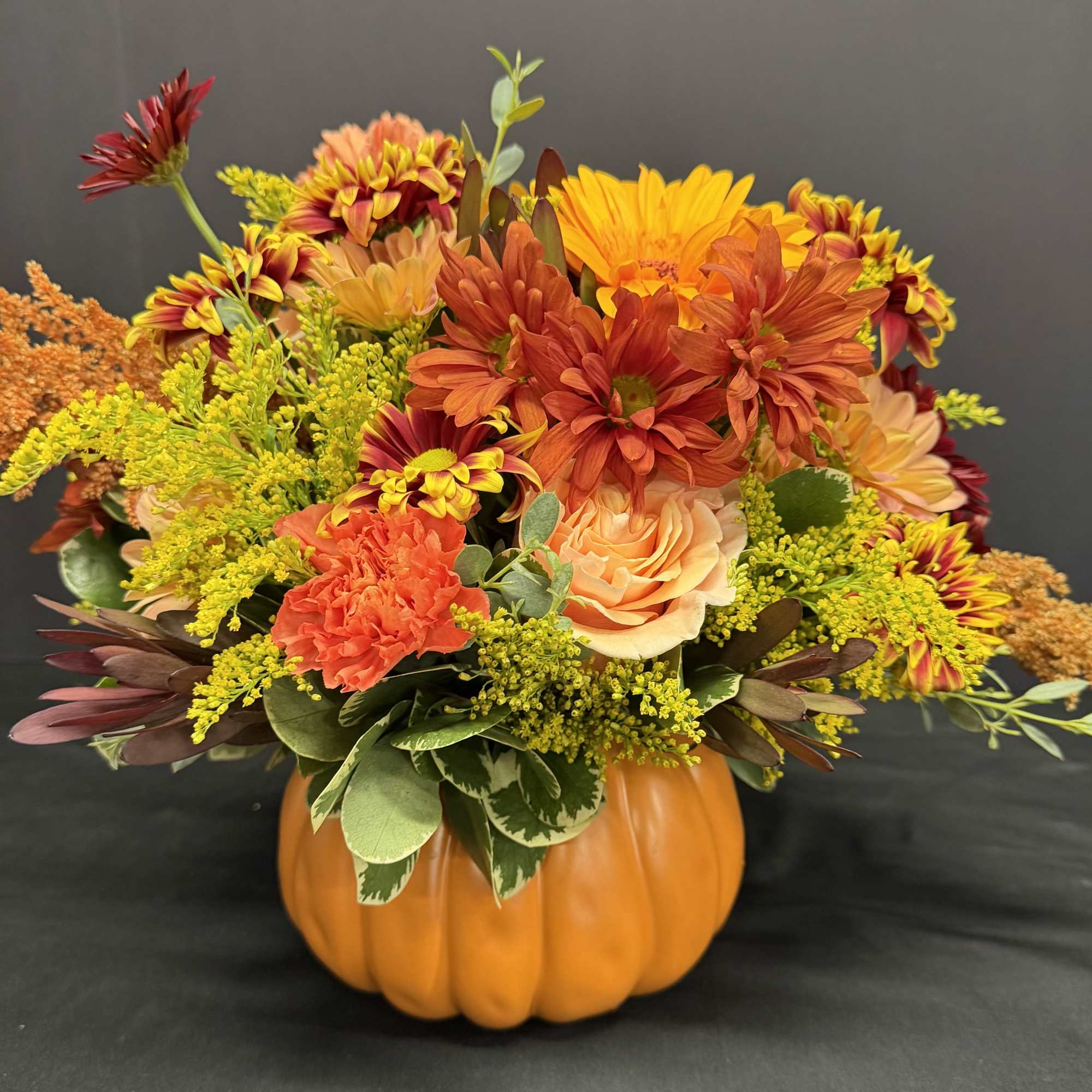 Autumn floral arrangement in a pumpkin container with orange, yellow, and red blooms
