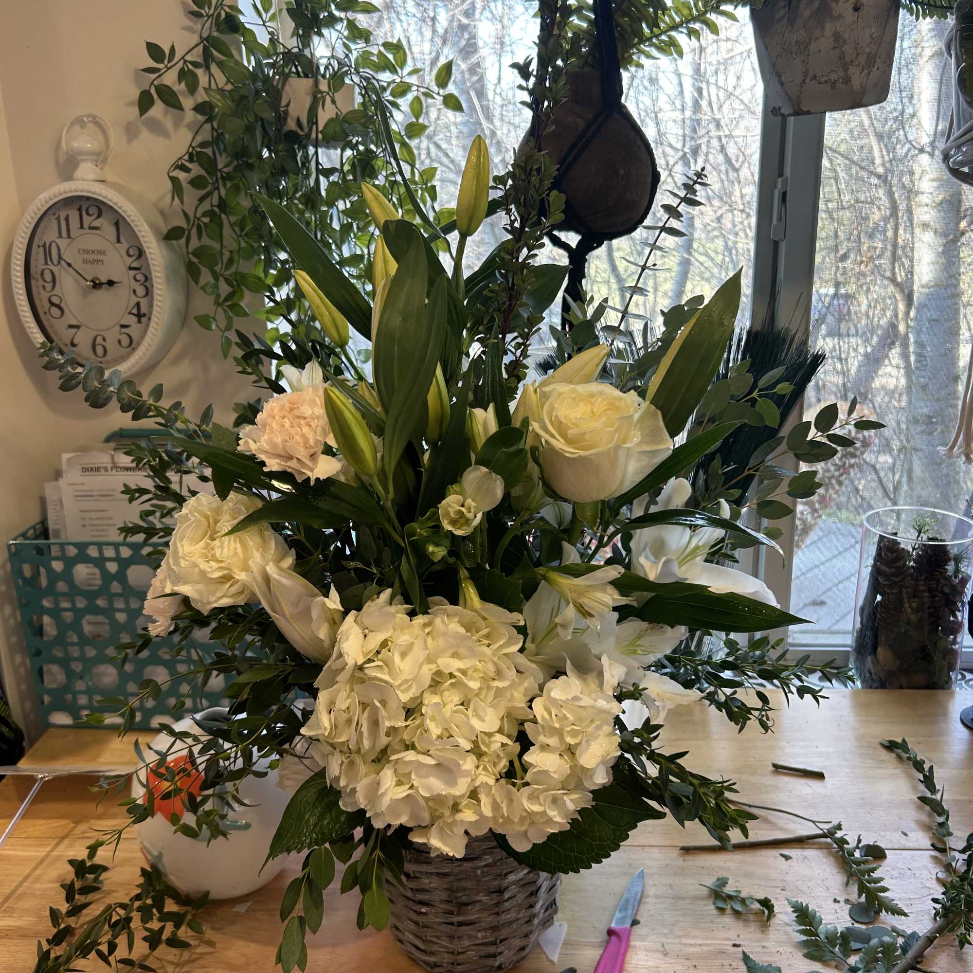White floral arrangement with roses, hydrangeas, and lilies in a woven basket