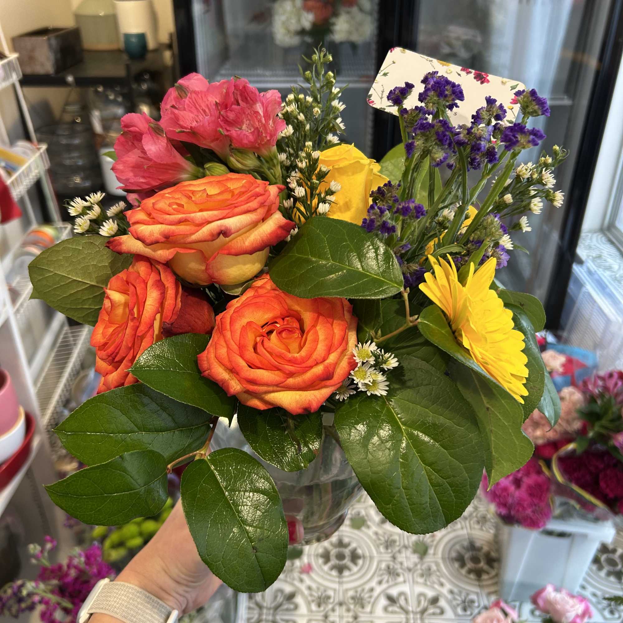 Bouquet of orange roses, pink alstroemeria, and yellow daisy flowers in a glass vase