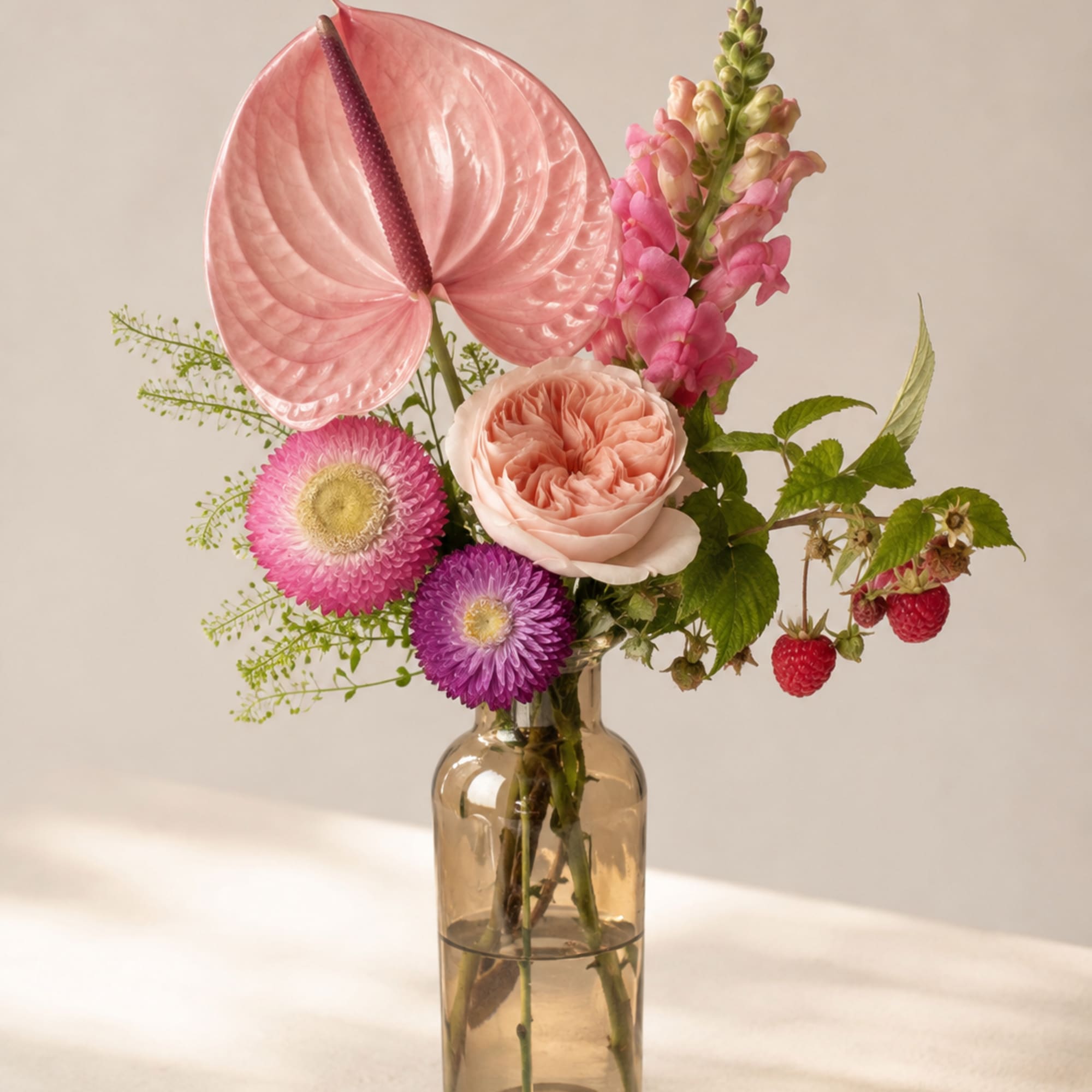 Pink floral arrangement in a glass vase with anthurium, roses, and snapdragons