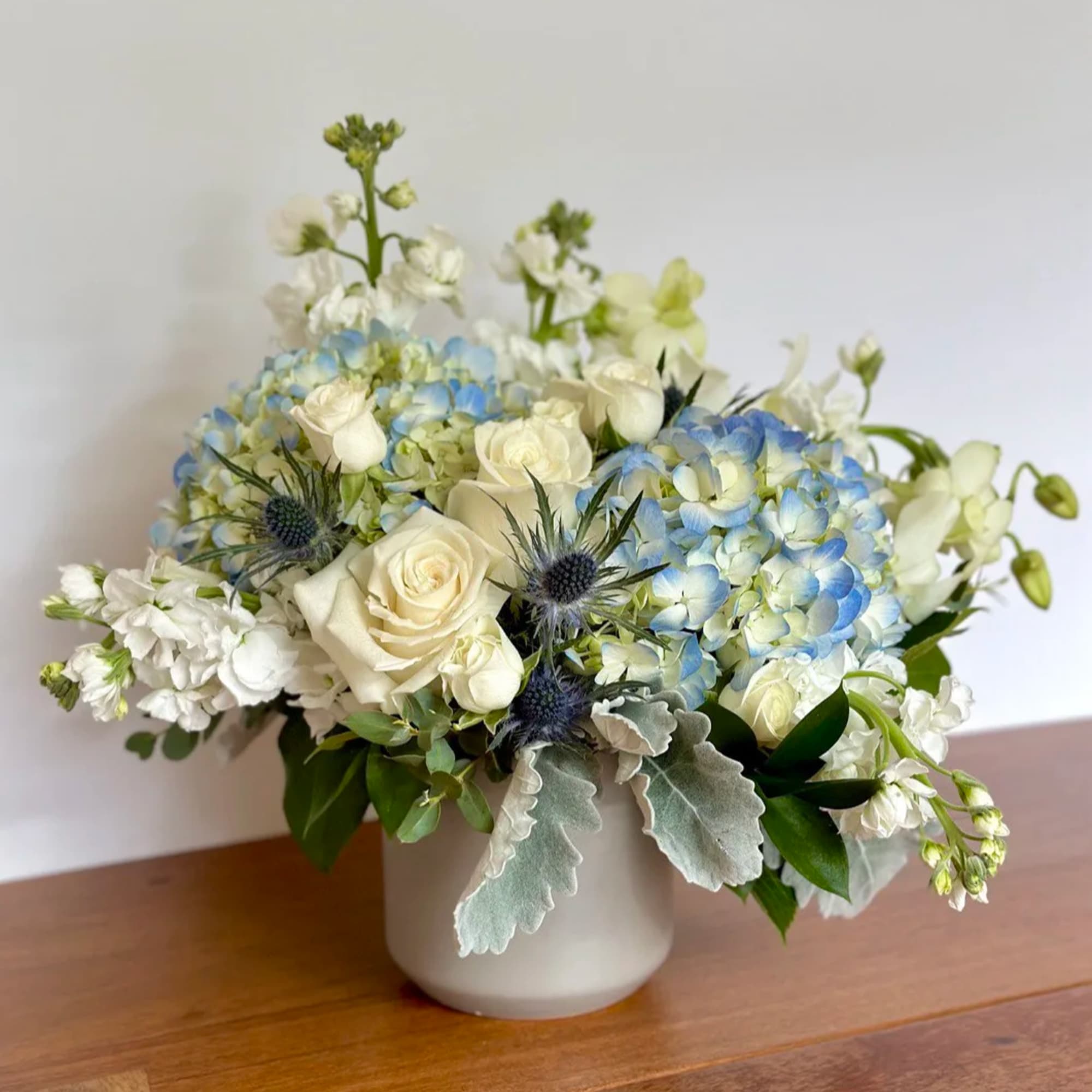 White roses and blue hydrangeas arranged in a white vase