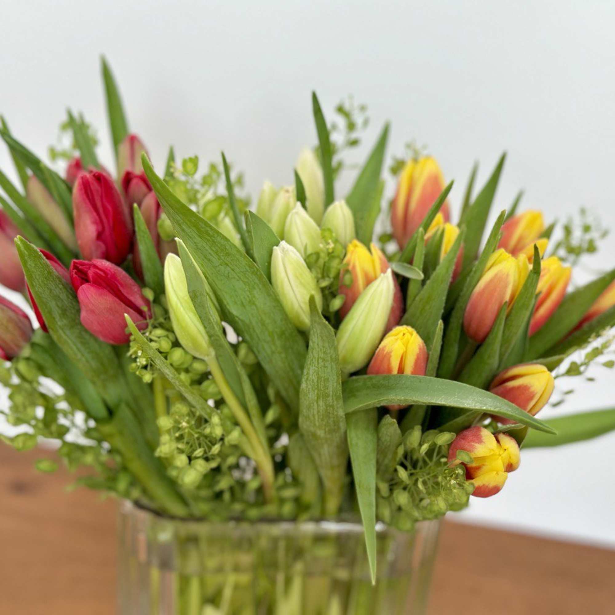 Bouquet of red, yellow, and white tulips in a clear glass vase, photo 3 of 3