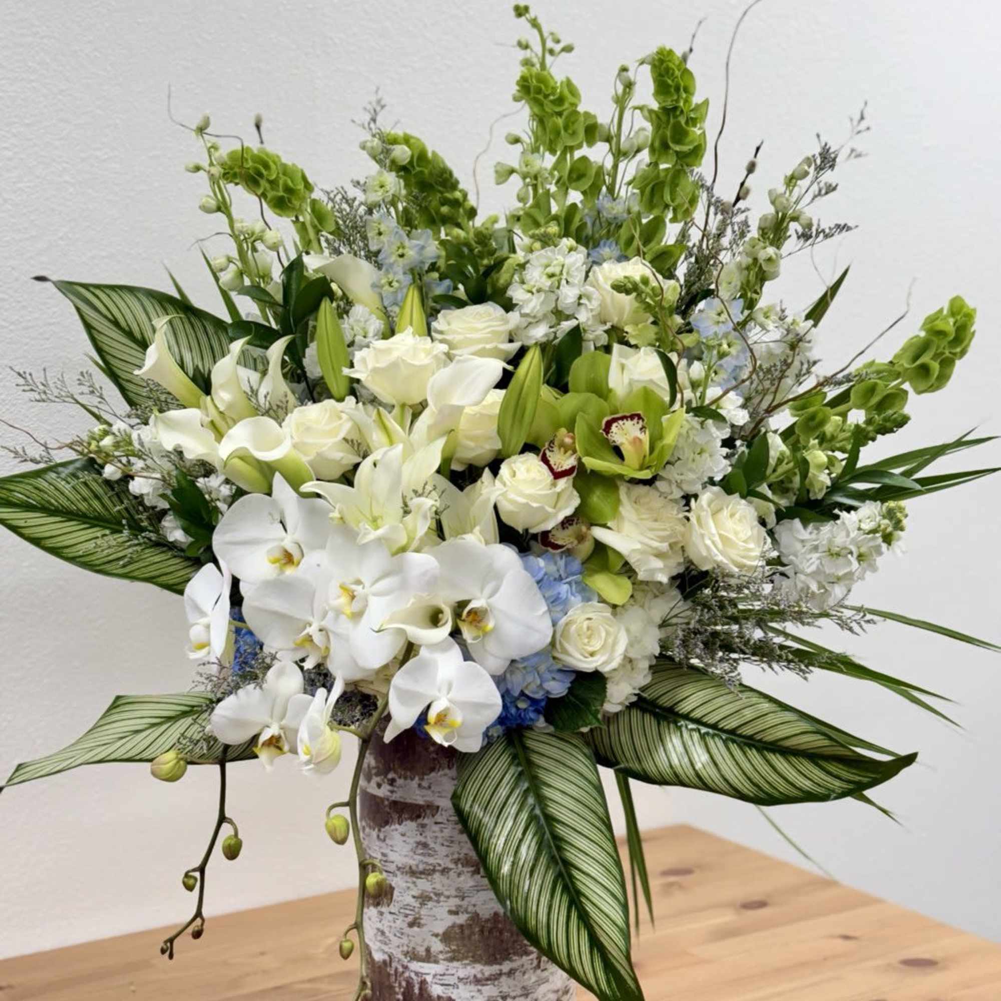 Tall arrangement of white orchids, roses, lilies, and green orchids in a rustic cylinder vase