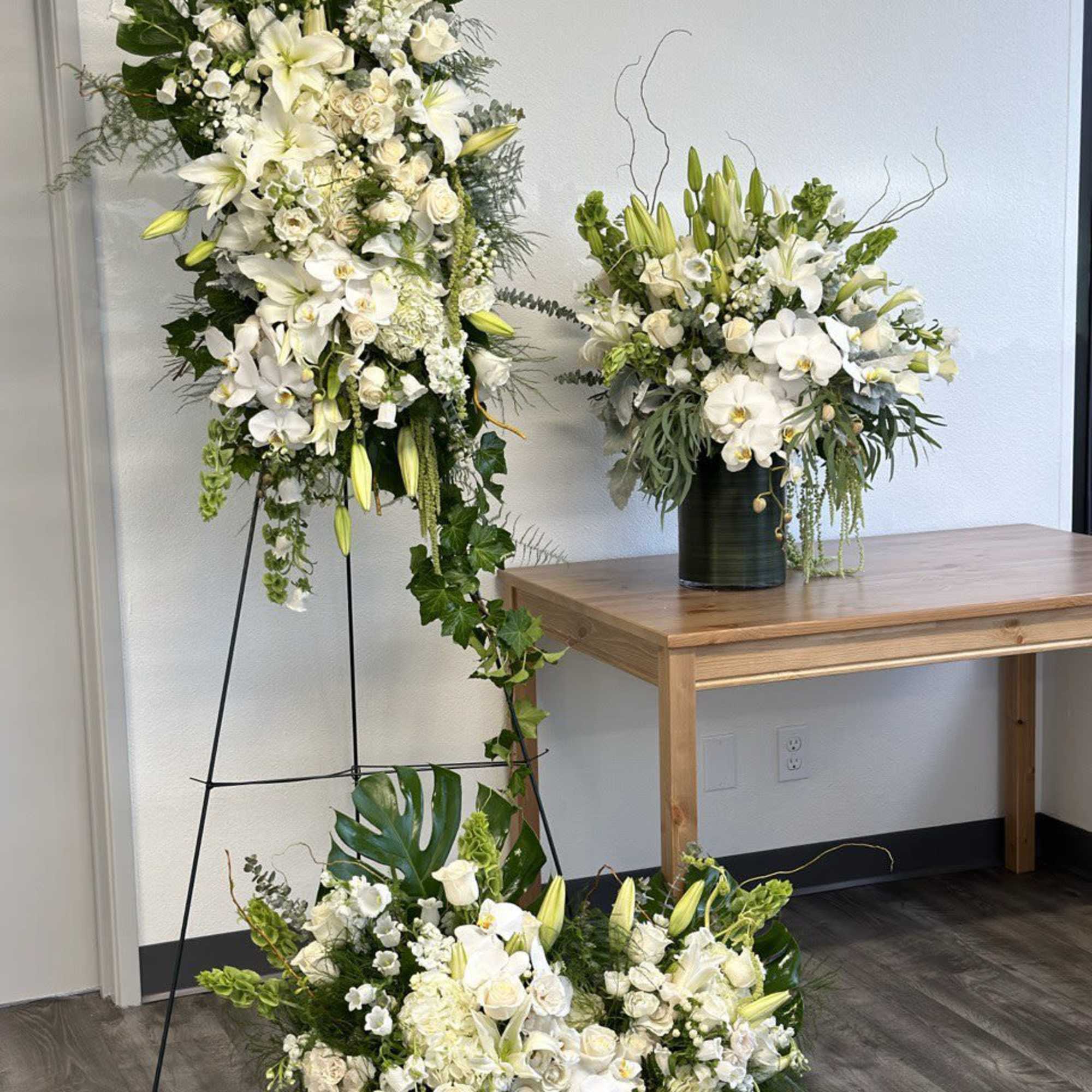 Three white floral arrangements with lilies and orchids in a room