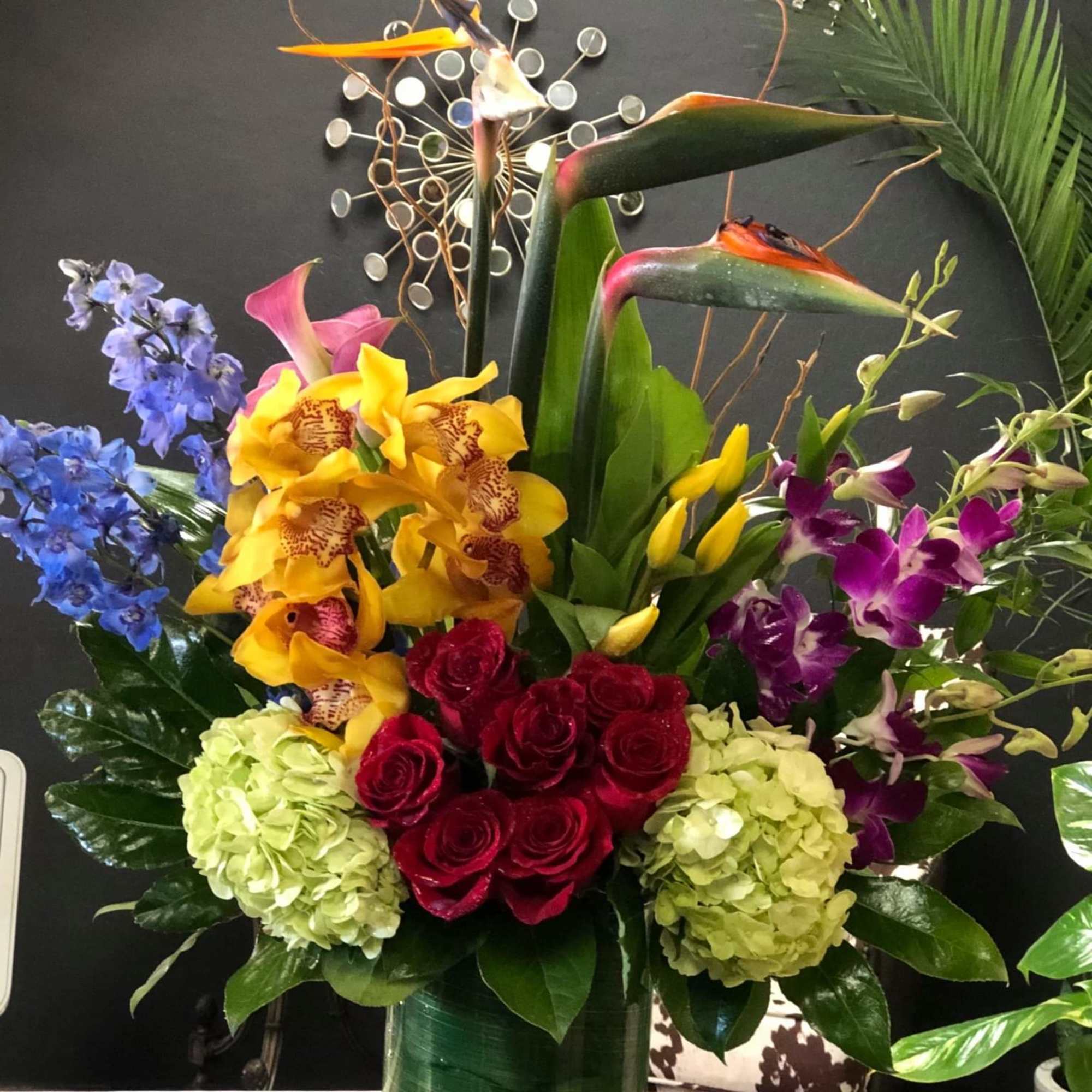 Tropical arrangement with orchids, roses, hydrangeas, and bird-of-paradise in a tall vase