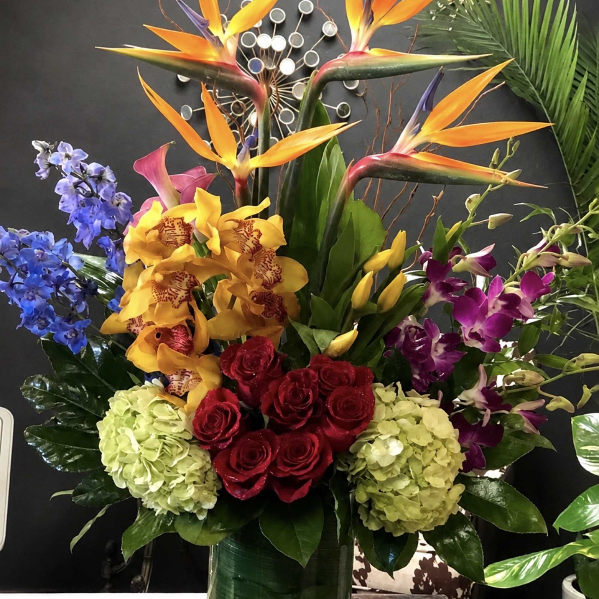 Tropical bouquet with bird of paradise, orchids, roses, and hydrangeas in a tall vase.