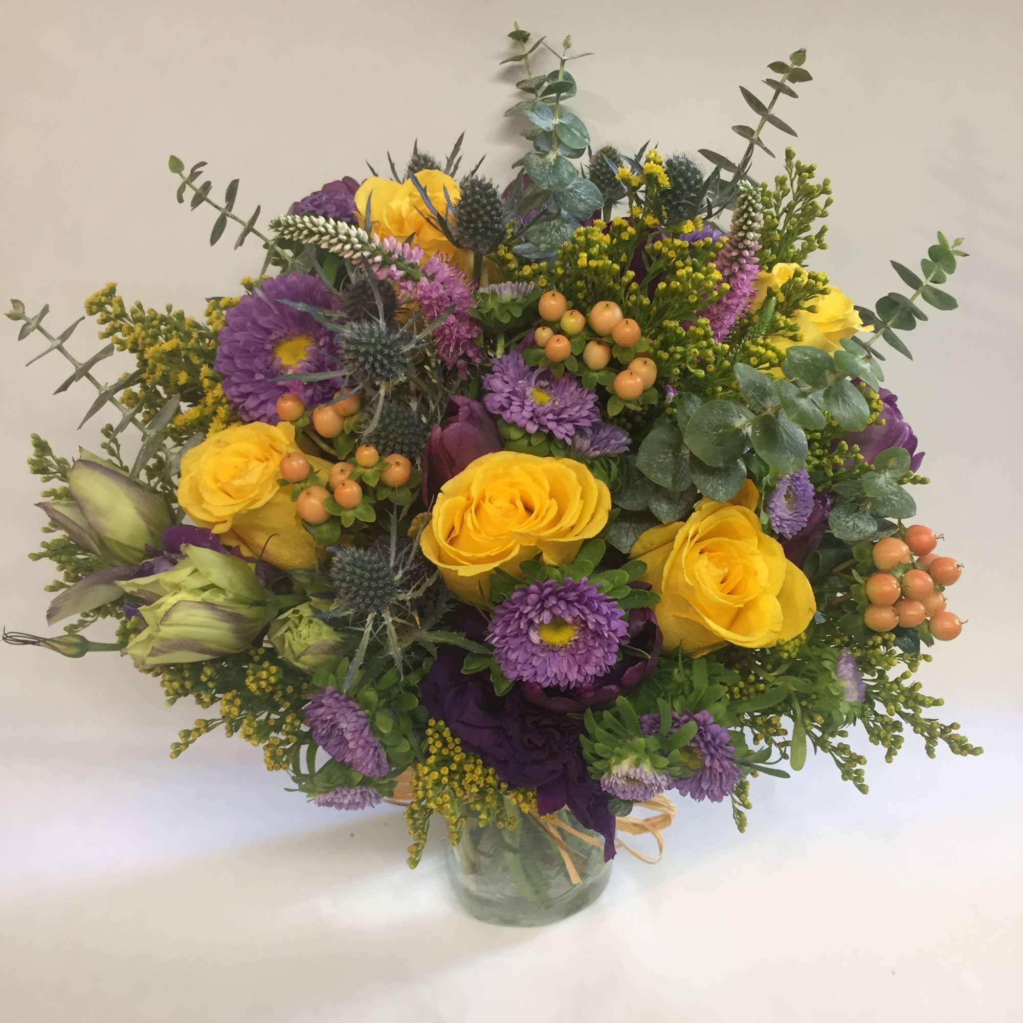 Bright bouquet of yellow roses and purple blooms in a clear glass vase