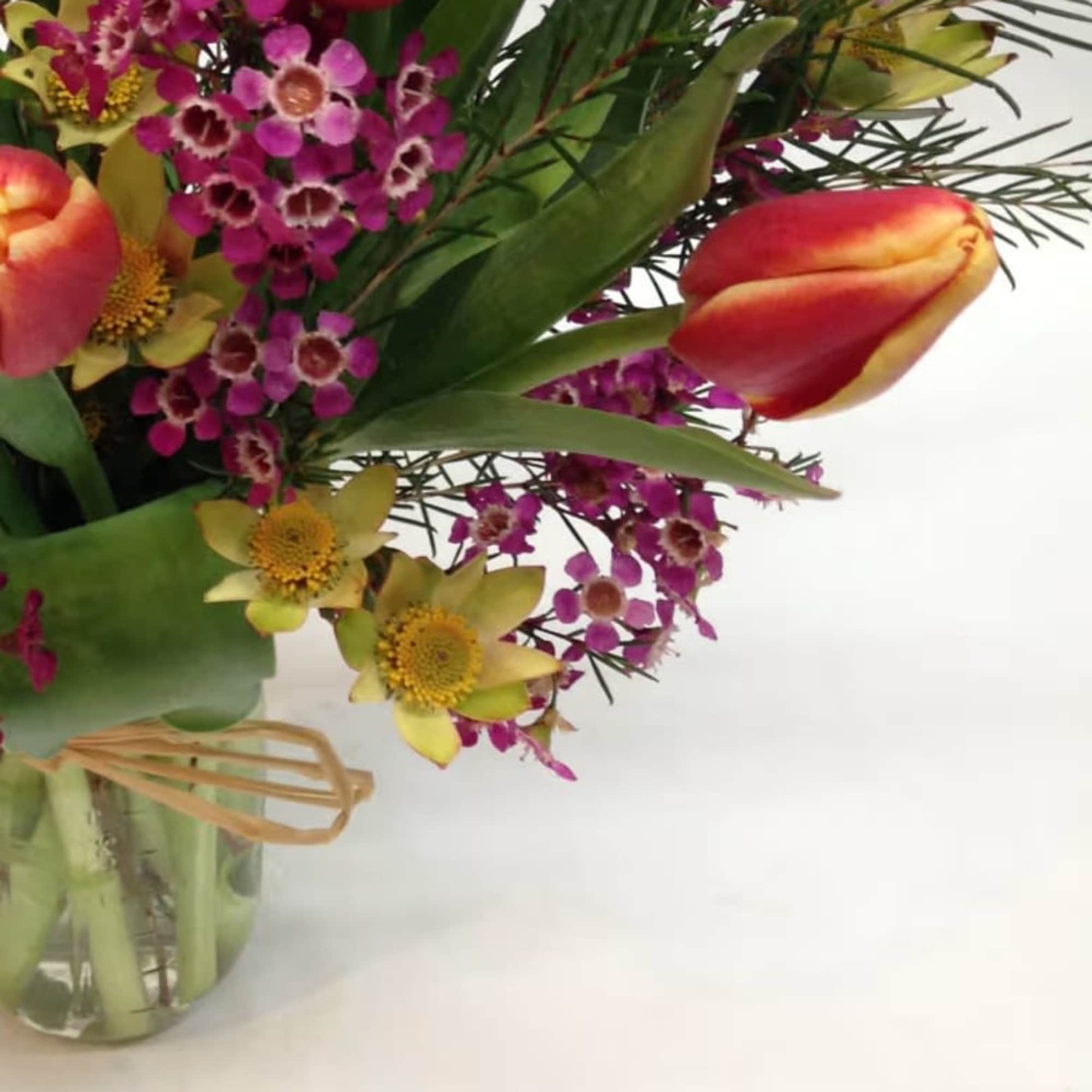 Bouquet with pink waxflowers and red-orange tulips in a glass vase