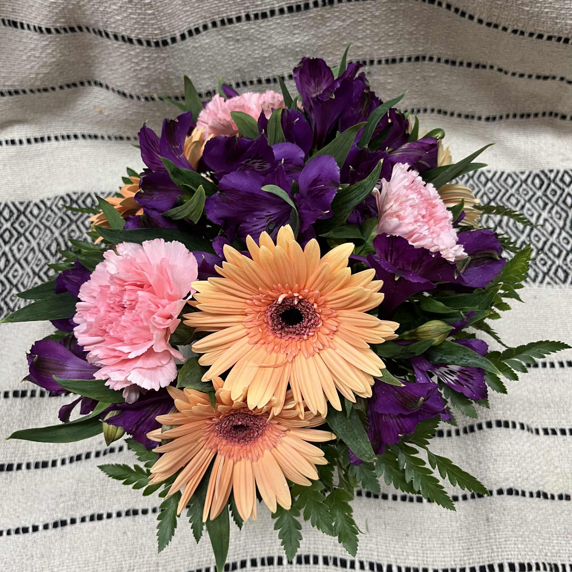 Bouquet of peach gerbera daisies, pink carnations, and purple flowers