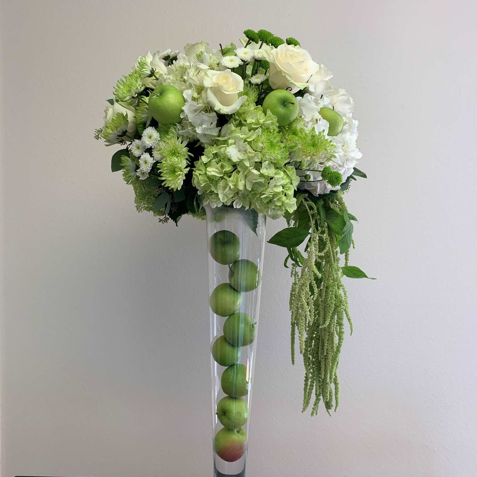 White and green floral arrangement in a tall clear vase with apples inside
