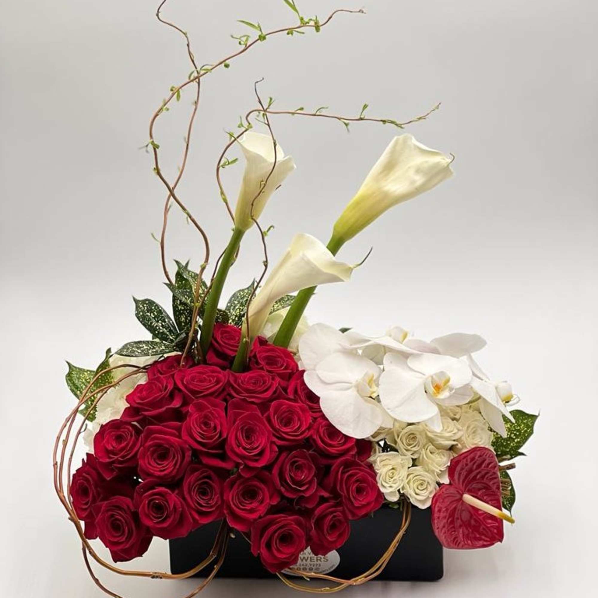 Red roses with white calla lilies and orchids in a black container