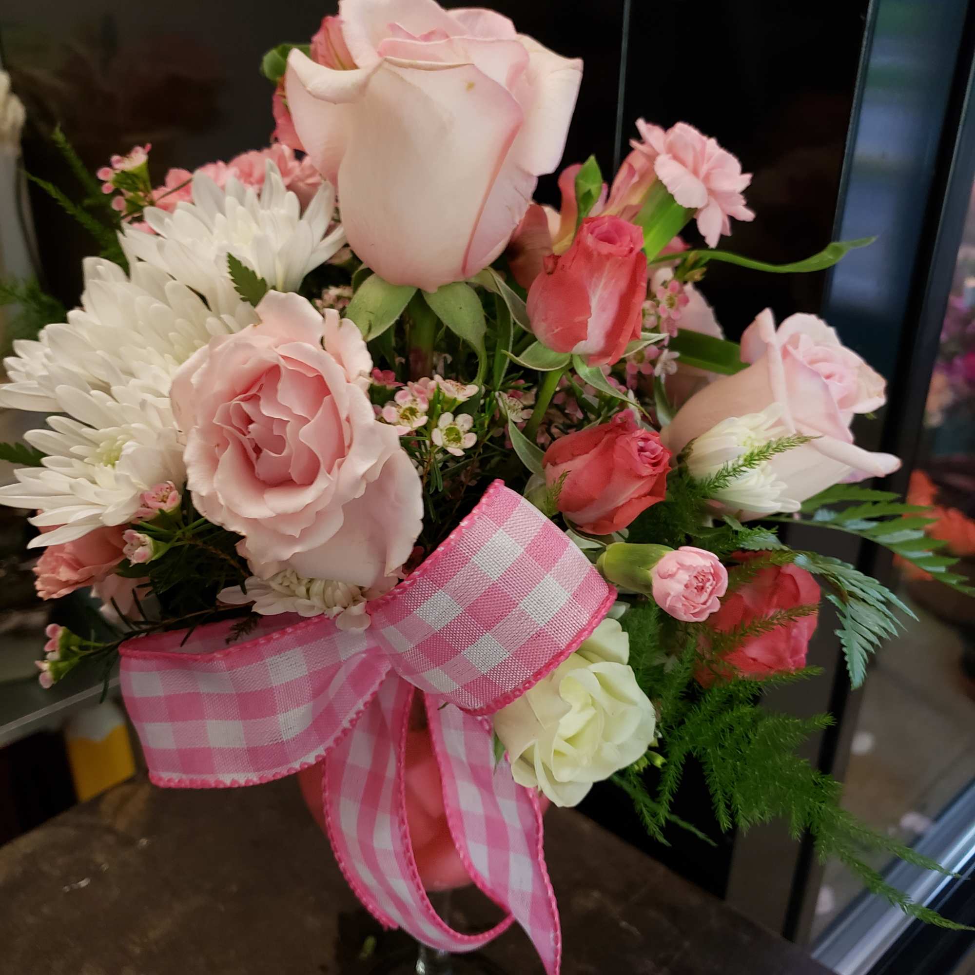 Pink and white rose bouquet in a glass vase with a gingham ribbon