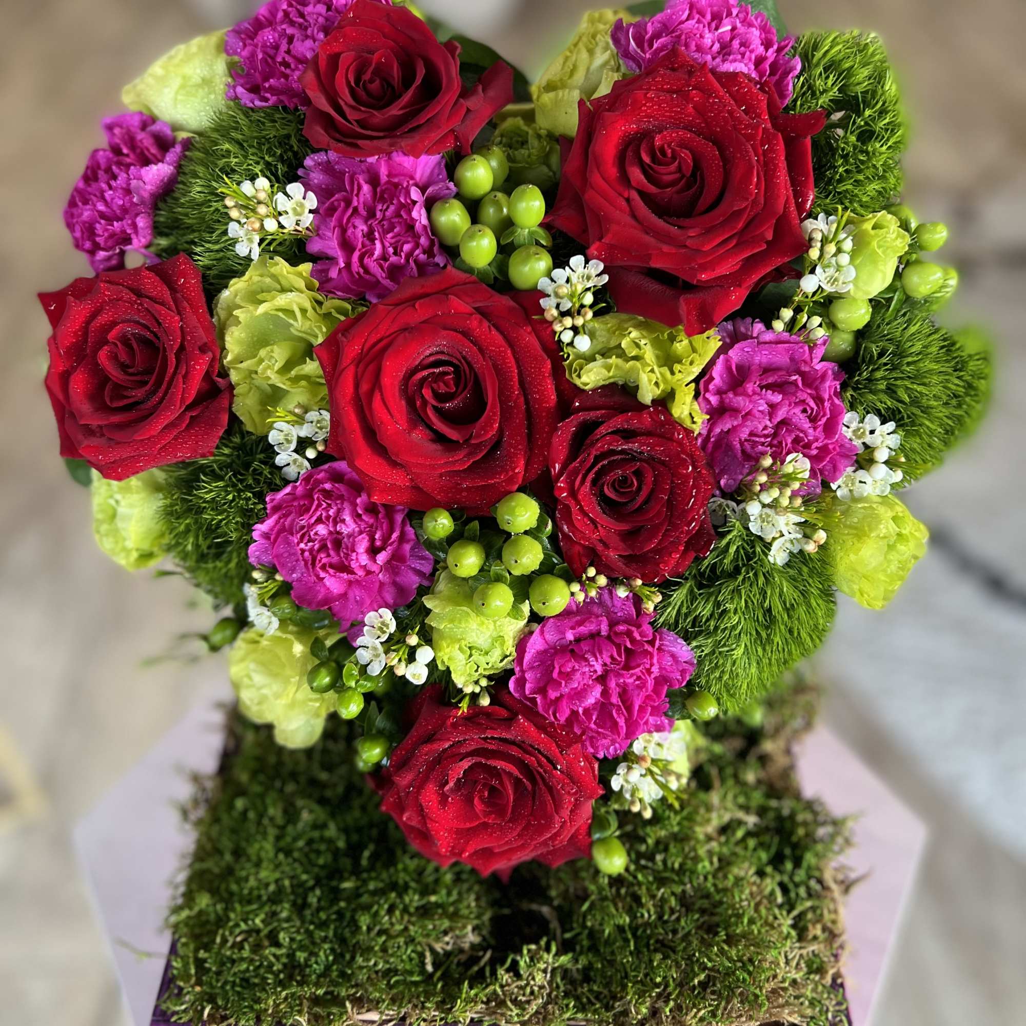 Heart-shaped bouquet of red roses, pink carnations, and green accents