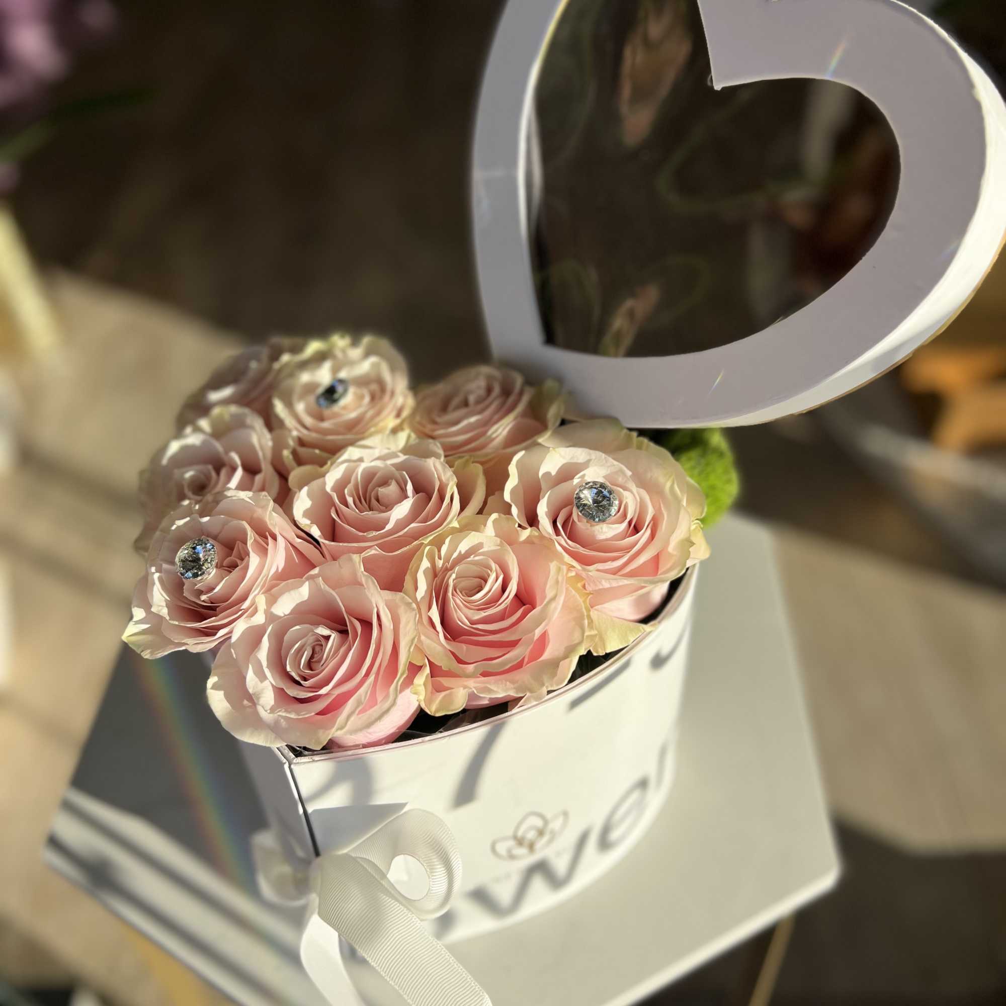 Pink roses in a white heart-shaped box with a ribbon bow