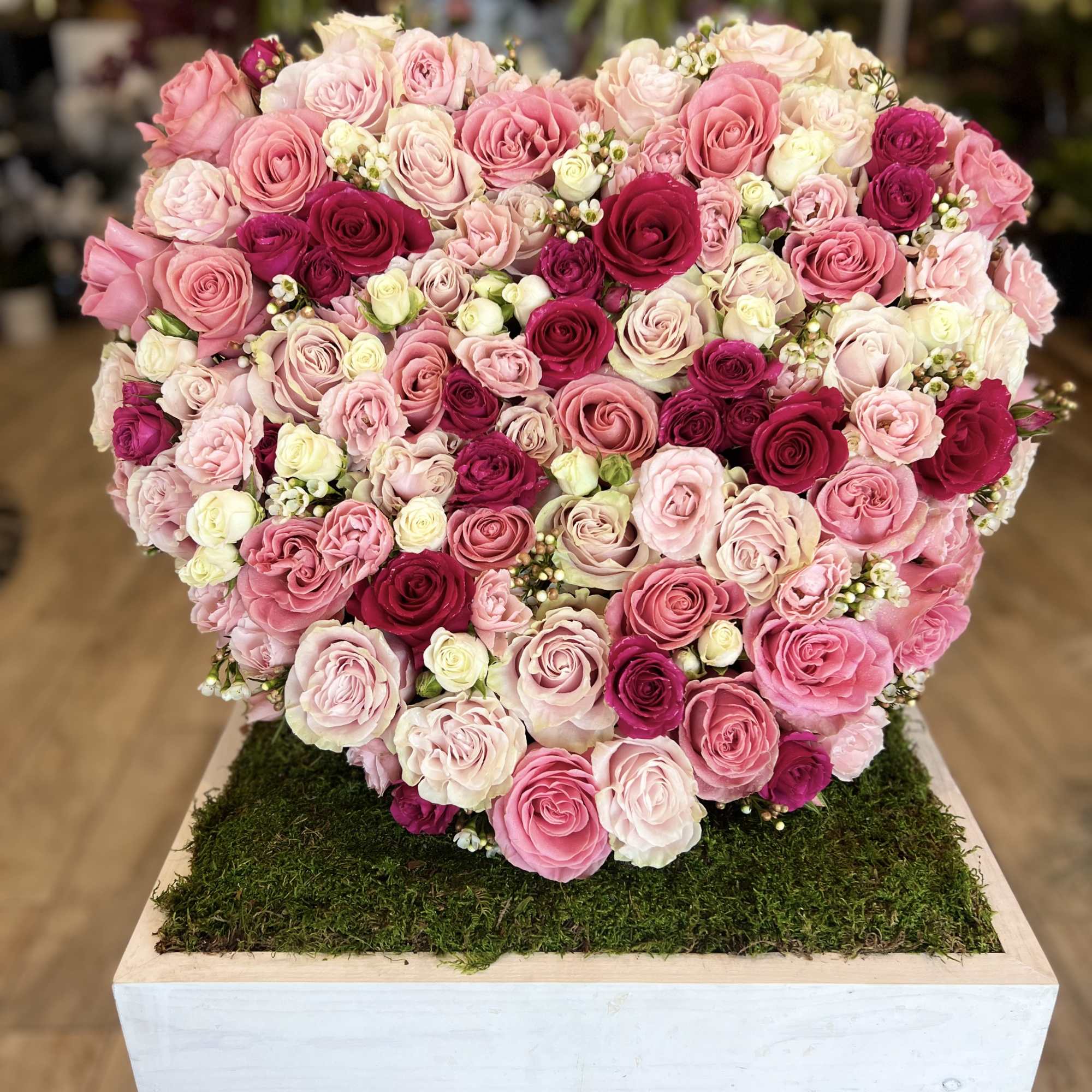 Heart-shaped arrangement of pink and white roses on a moss-covered base