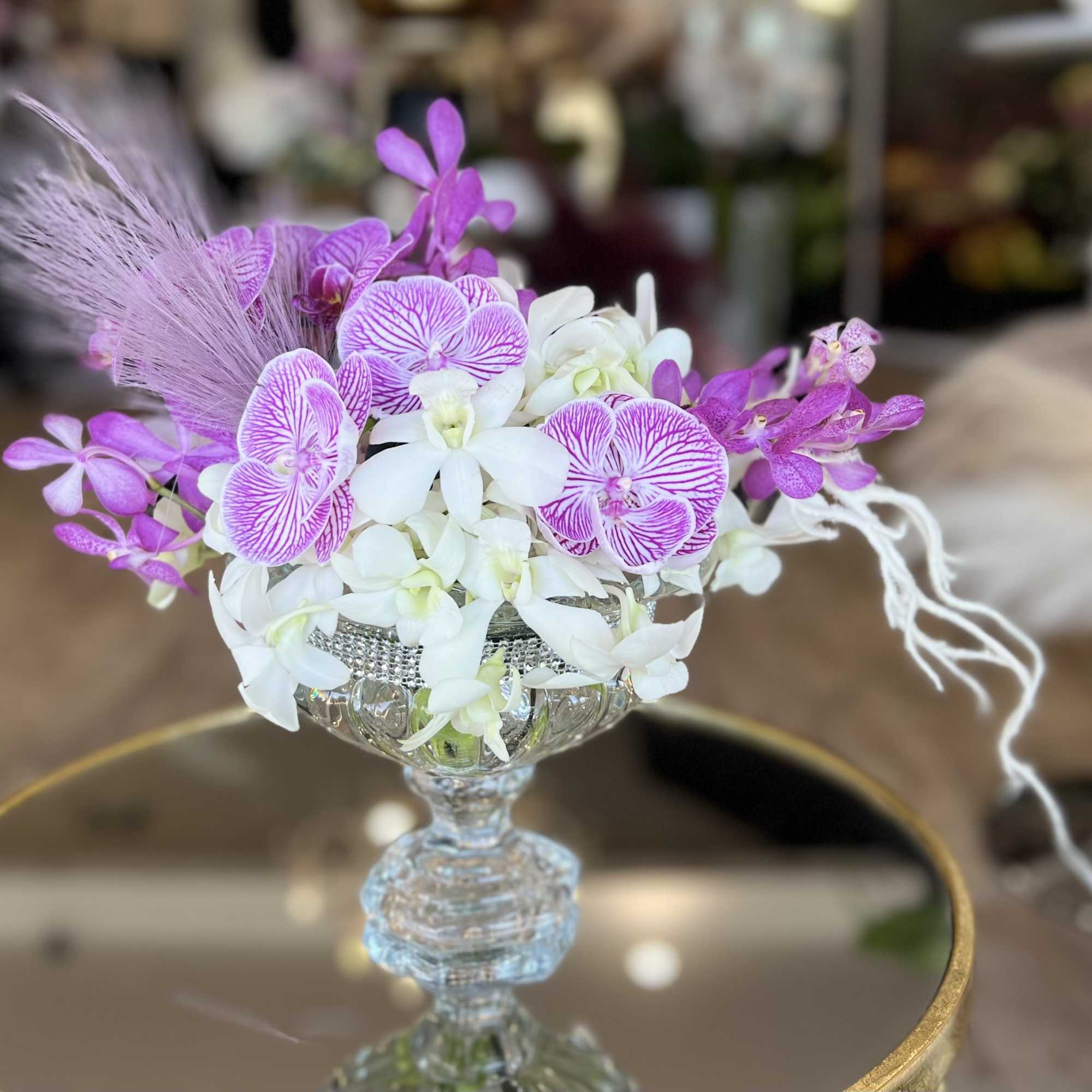 Pink and white orchid arrangement in a clear glass compote vase