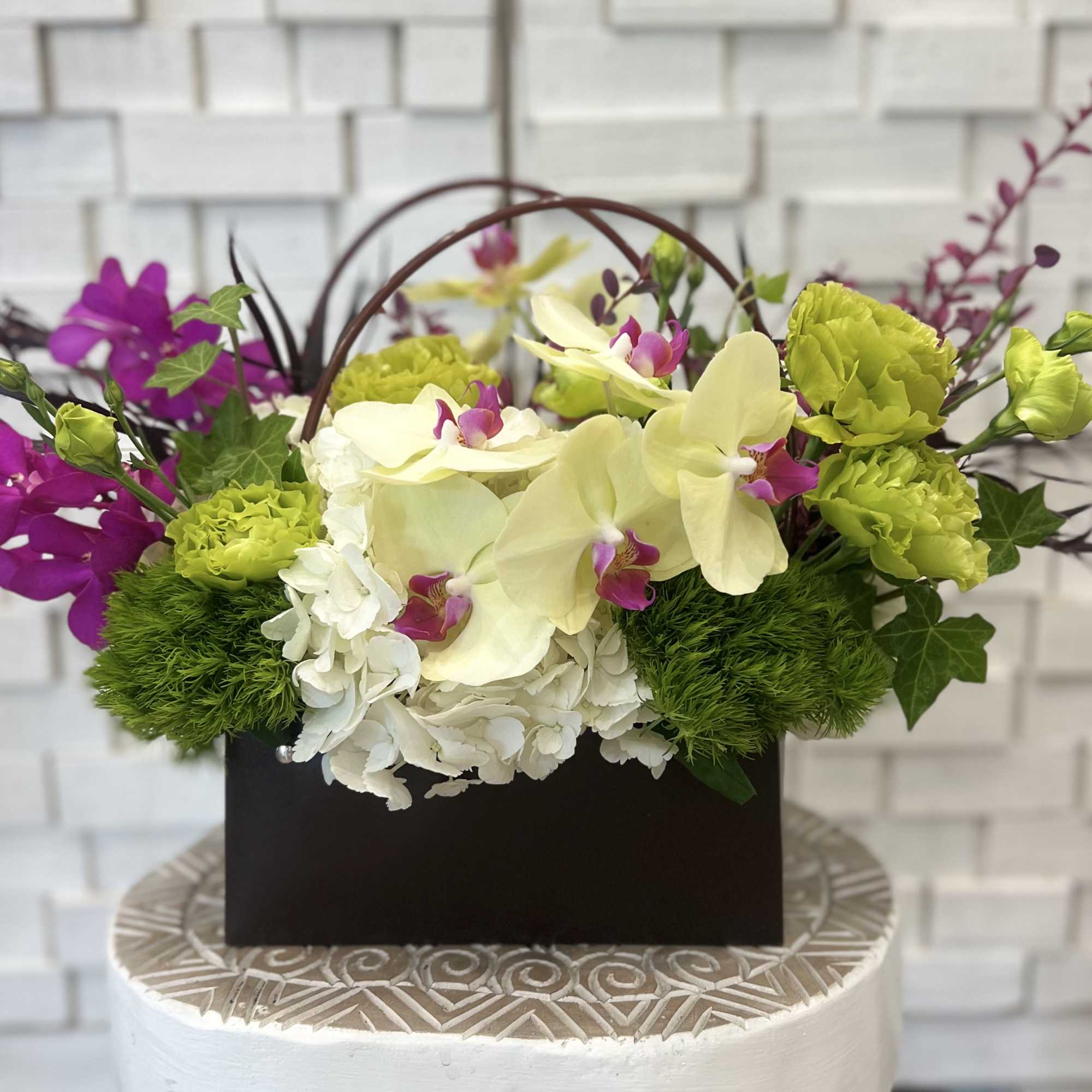 Floral arrangement with orchids, hydrangeas, and green carnations in a dark box