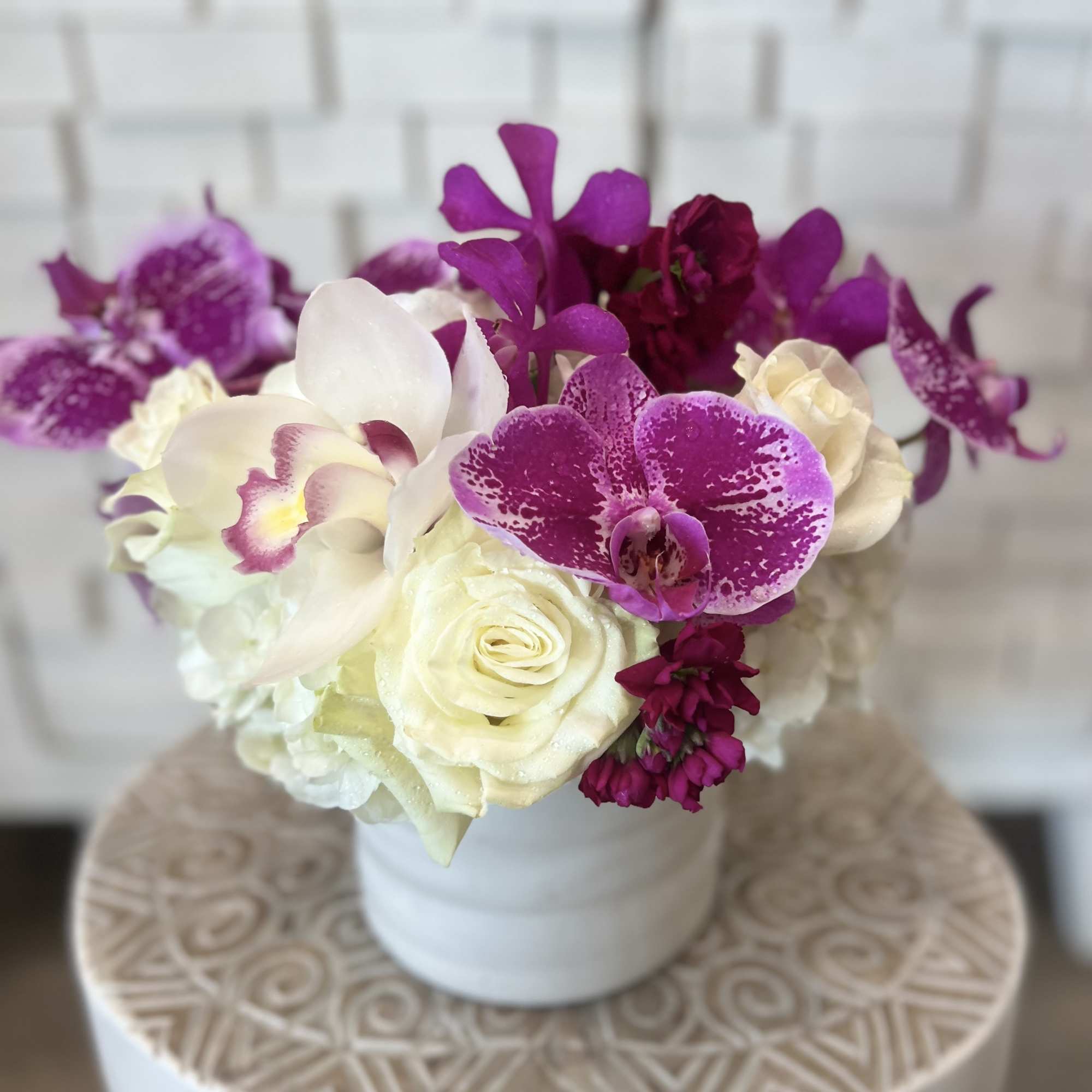 White roses and purple orchids arranged in a white vase